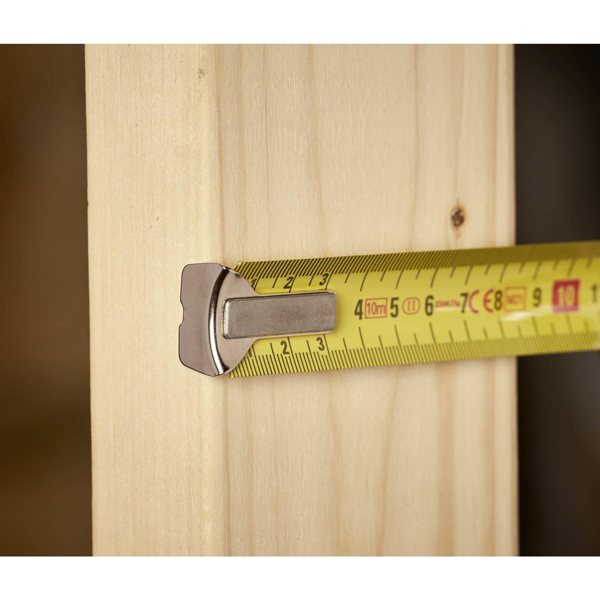 Een geel meetlint meet de breedte van een houten balk.