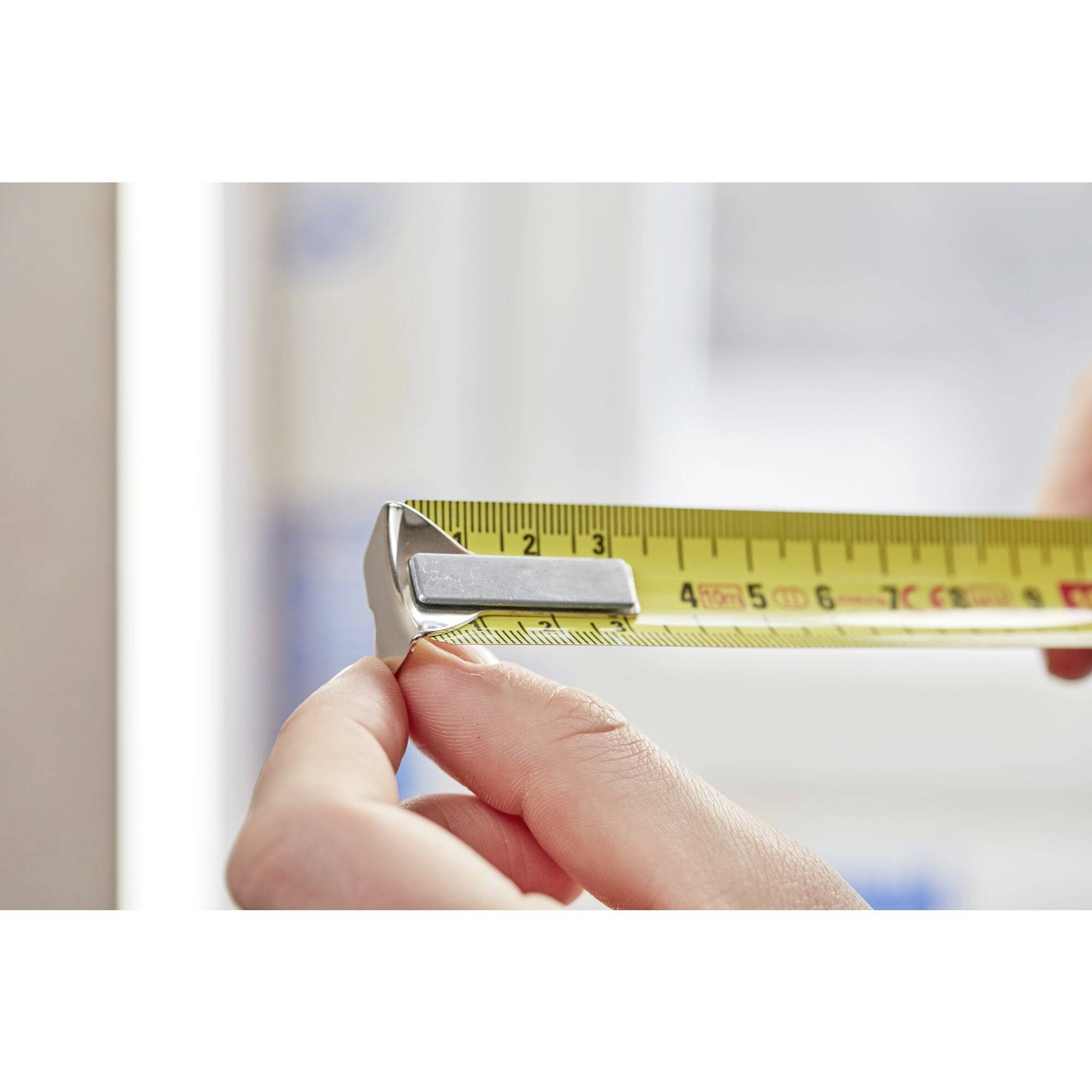 Twee handen houden een geel meetlint vast, dat is ingesteld op een lengte van ongeveer 2,5 cm.