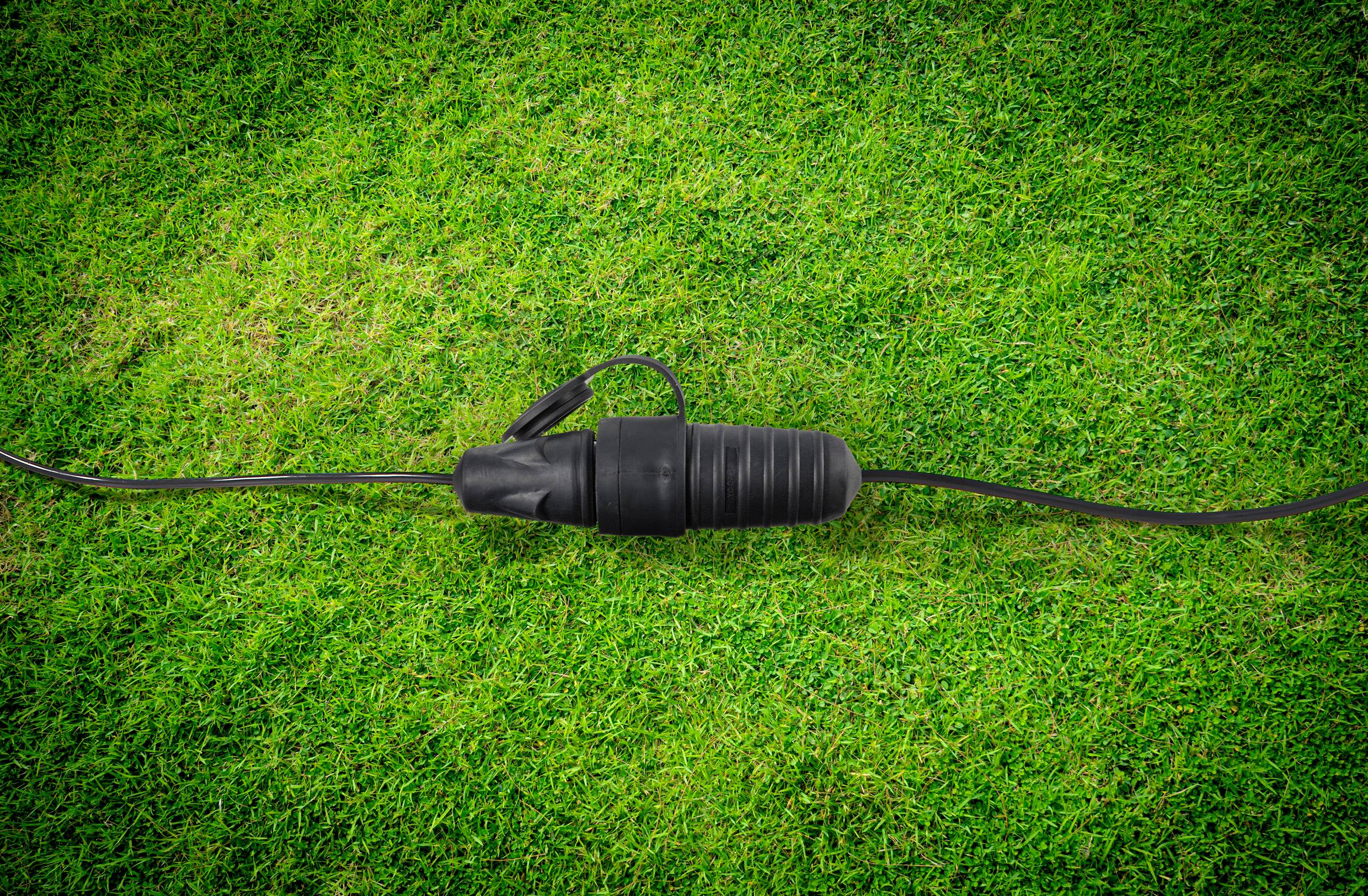 Een elektriciteitskabel met een zwarte stekker ligt op groen gras.