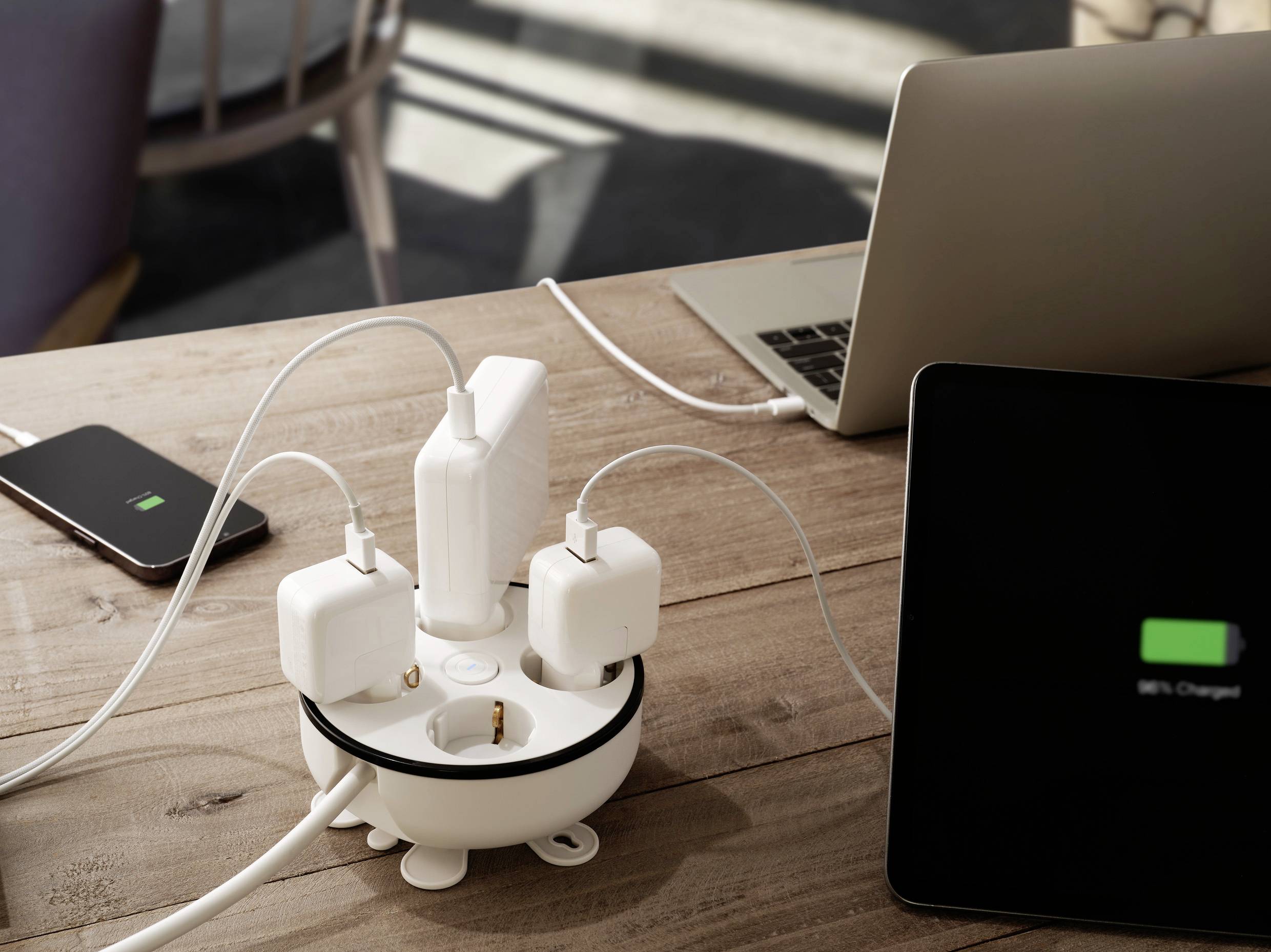 Een tafel met een laptop, een tablet en een smartphone die zijn aangesloten op een stekkerdoos. Alle apparaten worden opgeladen.