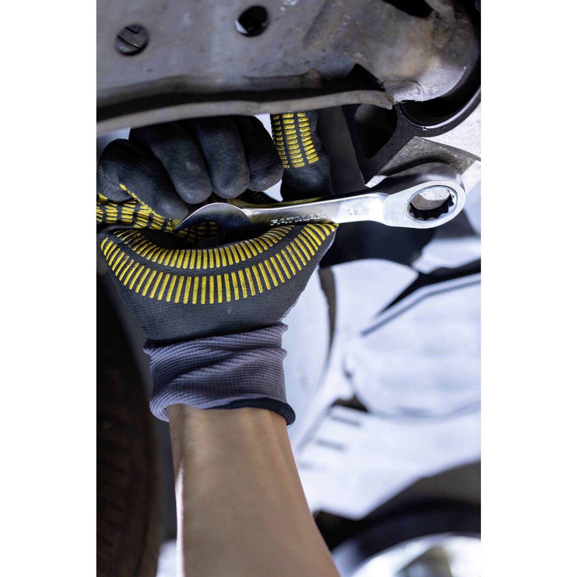 Close-up van een persoon die een schroef met een moersleutel vastdraait onder een voertuig, terwijl ze werkhandschoenen dragen.