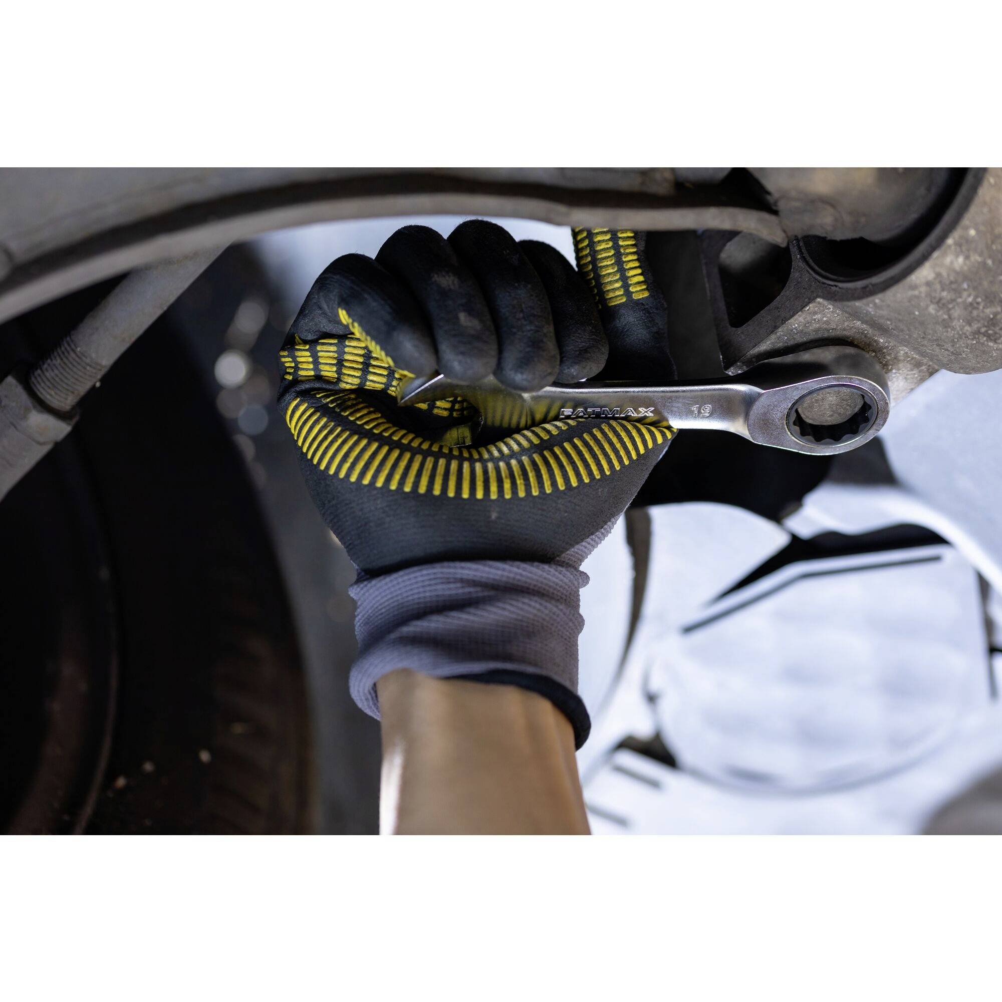 Een persoon draagt werkhandschoenen en gebruikt een moersleutel om aan een autoonderdeel te draaien.