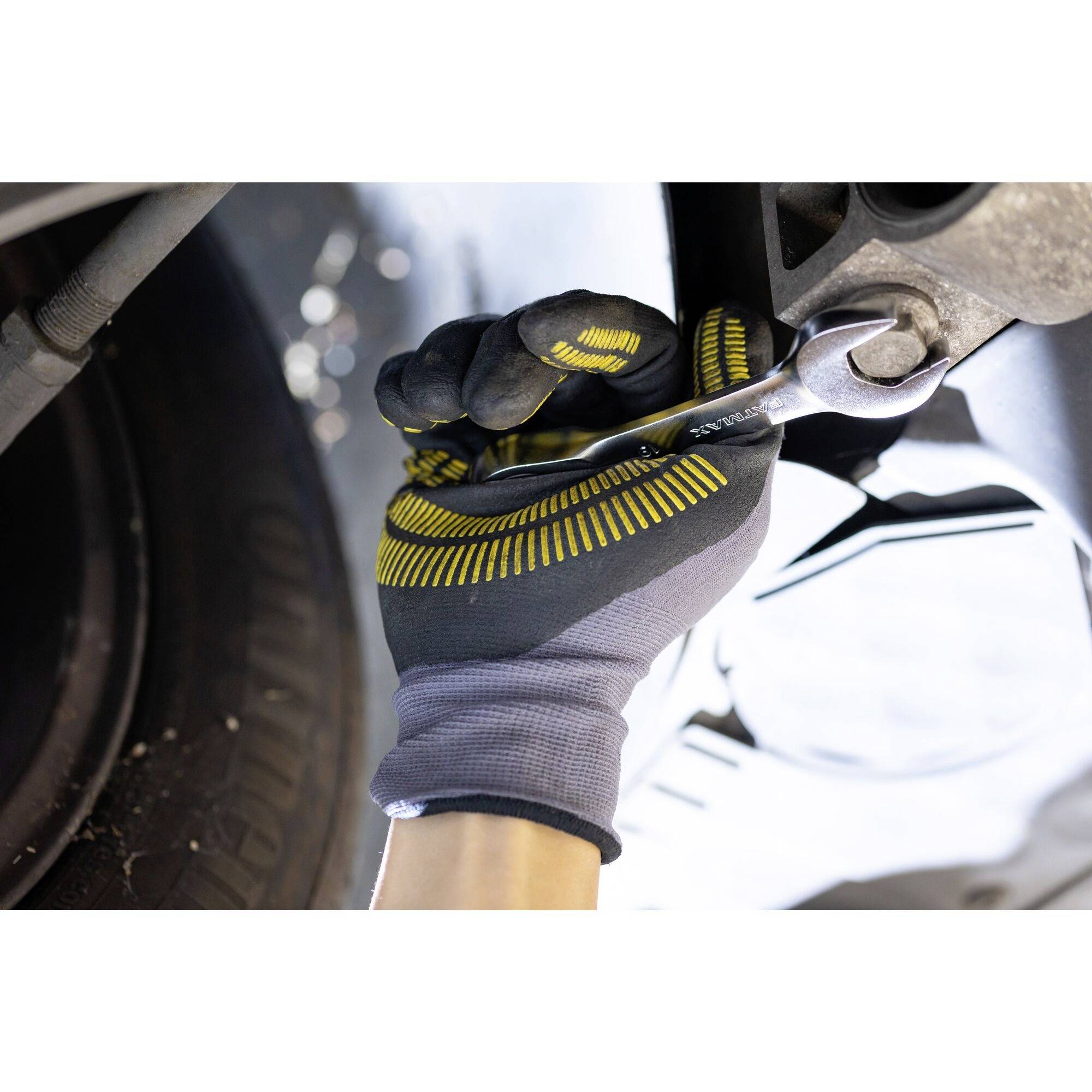 Een hand met een werkhandschoen houdt een moersleutel vast en draait een schroef aan op een voertuig.