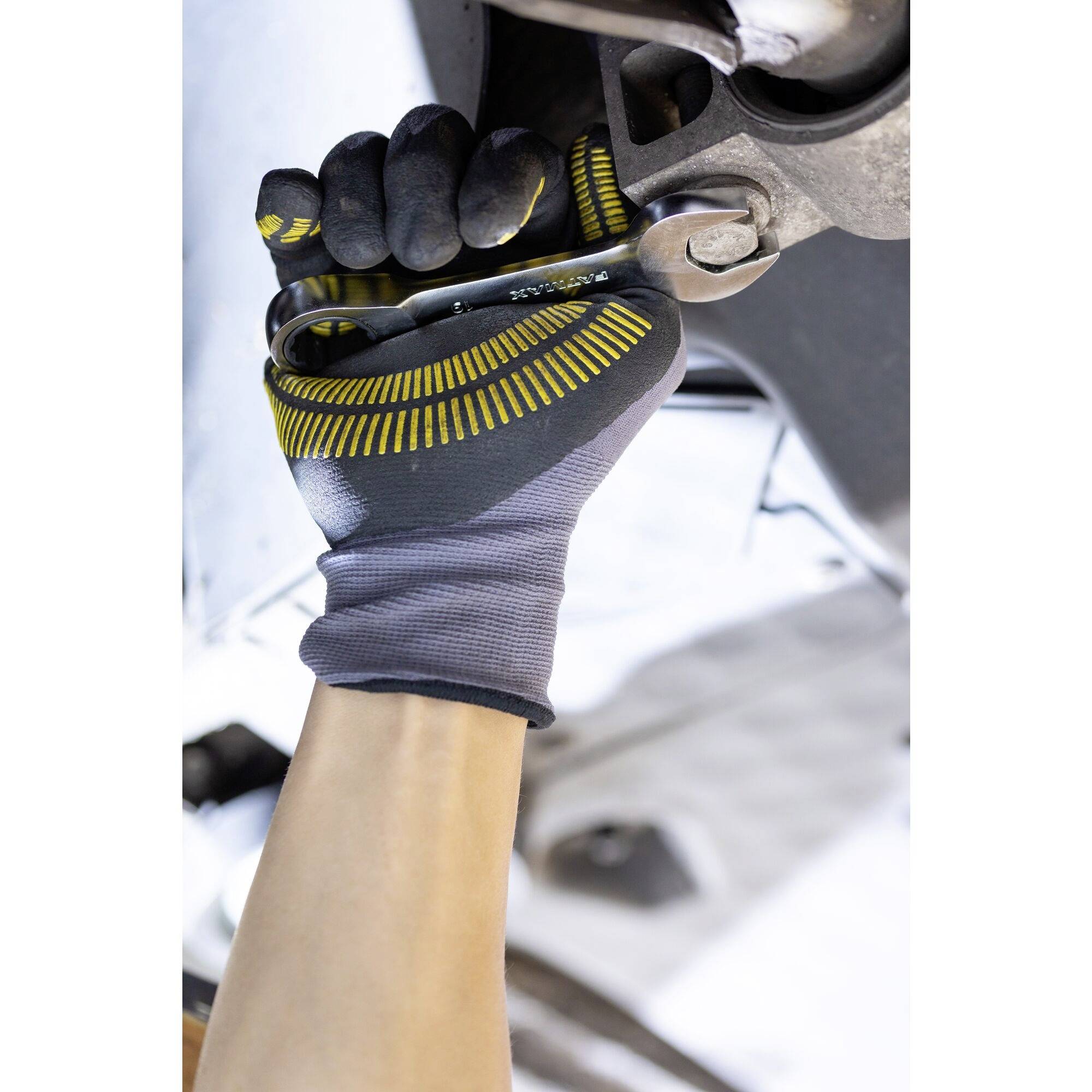 Hand in veiligheidshandschoen houdt moersleutel vast en draait moer aan onderzijde van voertuig.