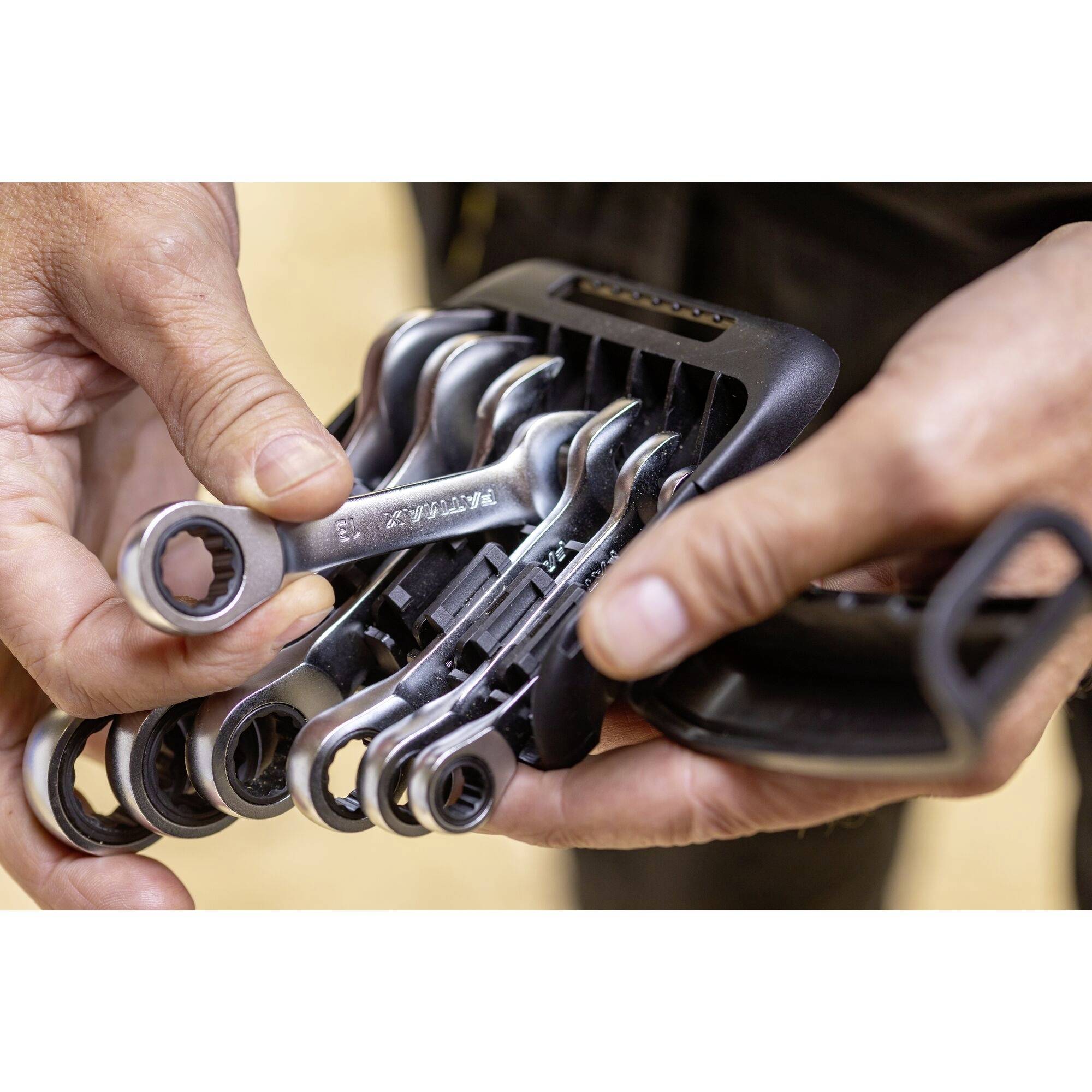 'Een set kleine moersleutels in verschillende maten wordt vastgehouden door twee handen. Ze zijn gerangschikt in een handige houder.'