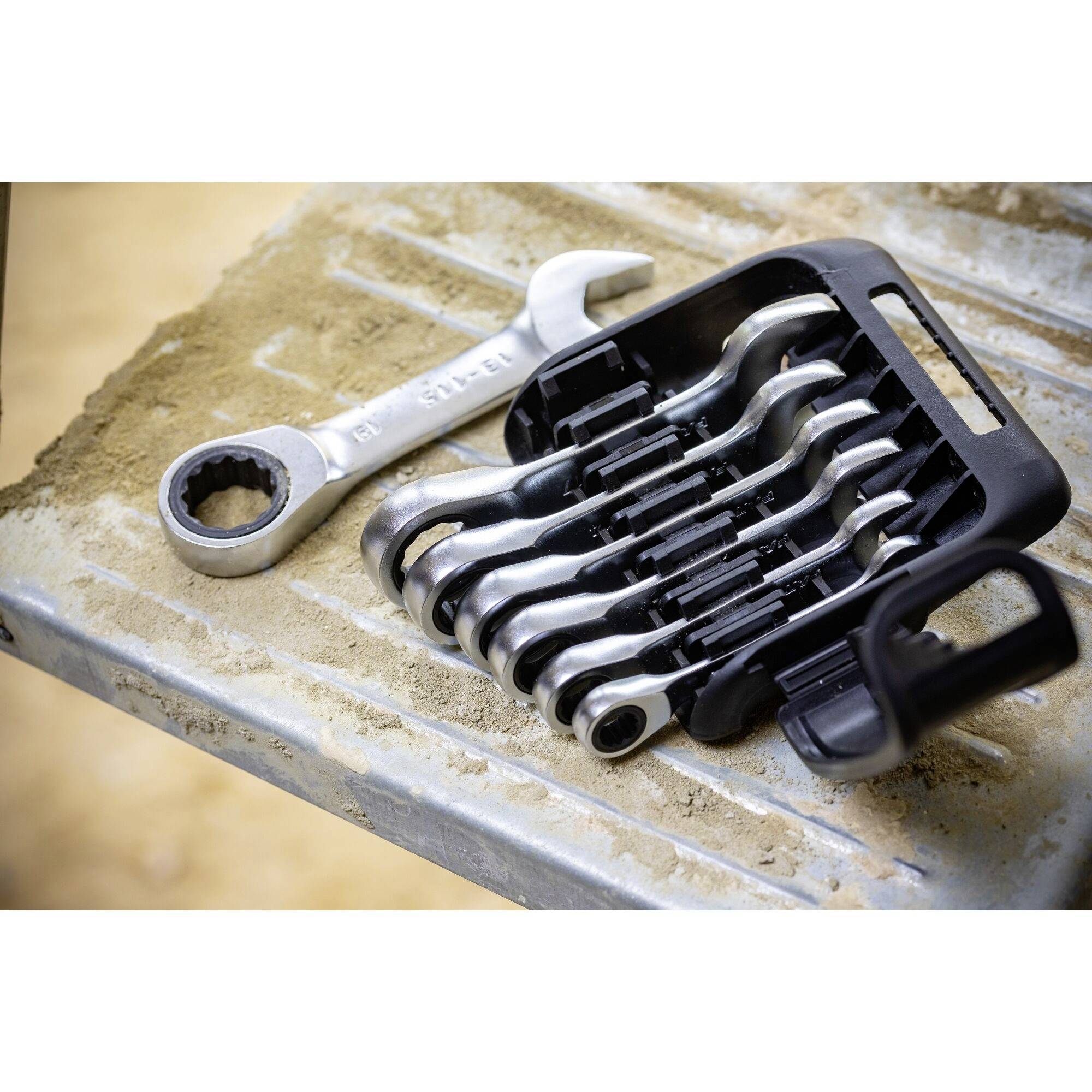 'Set van steek- en ringsleutels, gedeeltelijk in een zwarte houder, liggend op een stoffig metalen oppervlak.'