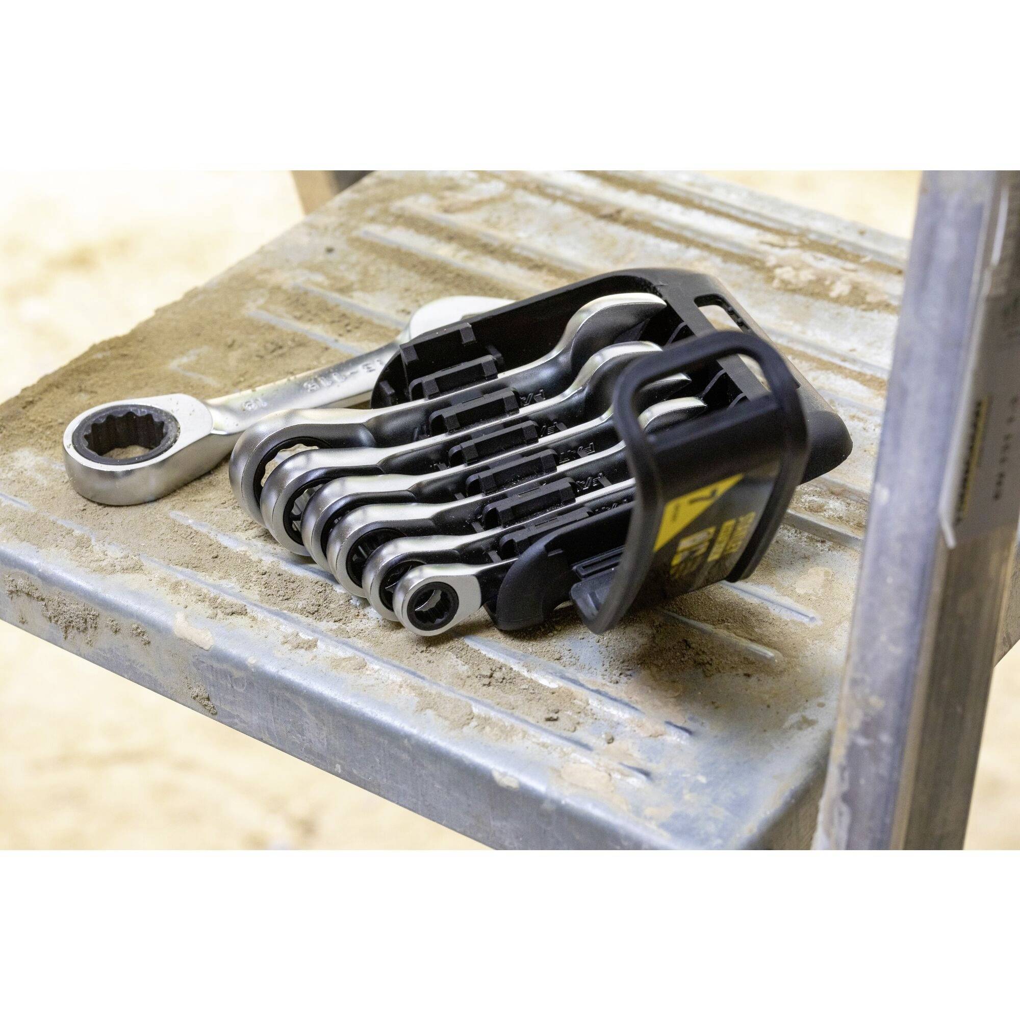 Een set steekringratelsleutels ligt op een metalen ladder. De sleutels zijn gerangschikt in verschillende maten en vastgemaakt in een zwarte houder.