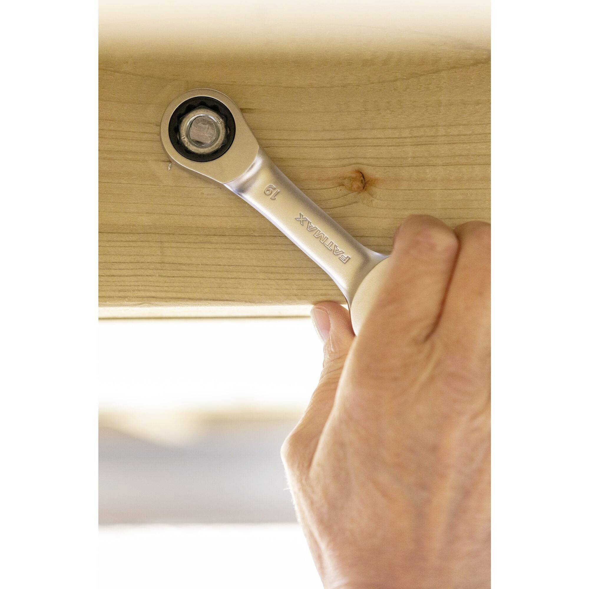 Een hand draait een schroef vast met een ringsleutel op een houten balk.