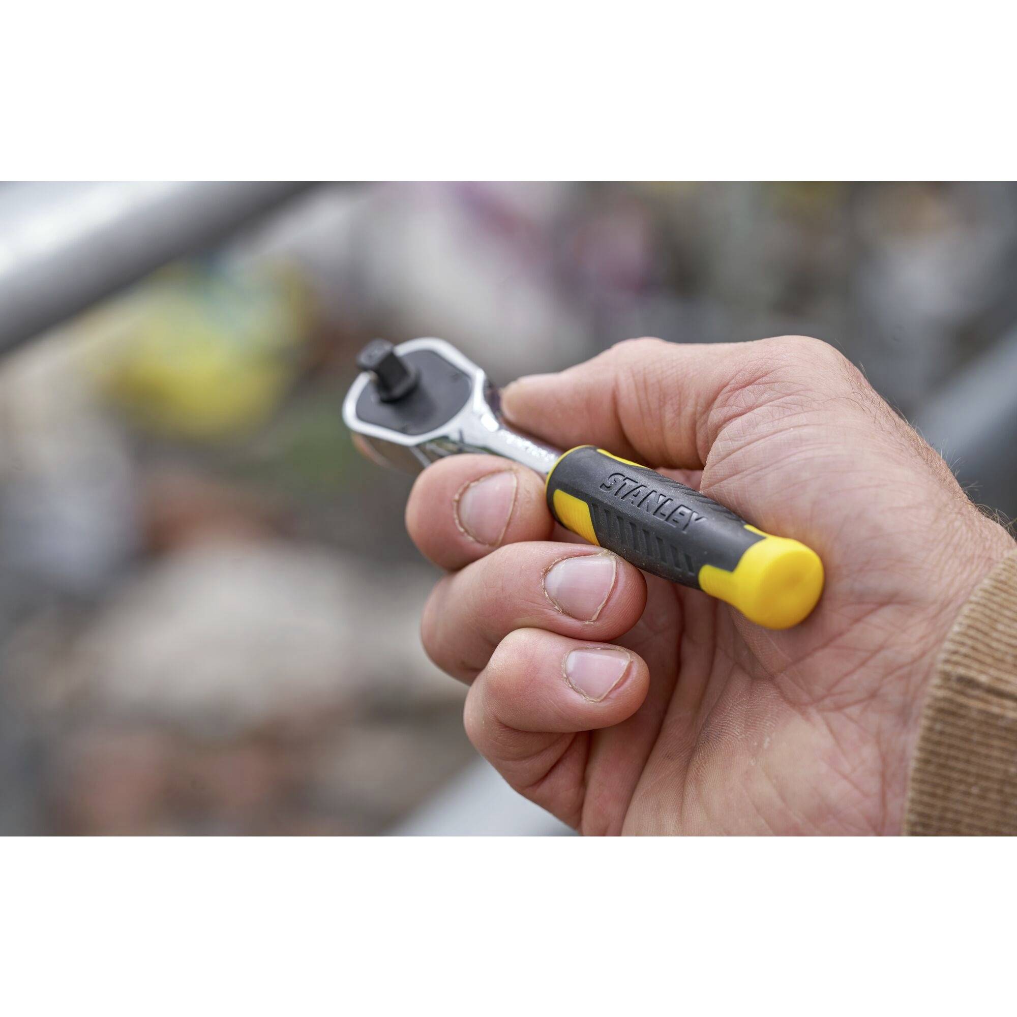 Een hand houdt een moersleutel vast met een geel en zwart handvat. Achtergrond wazig, focus op het gereedschap.
