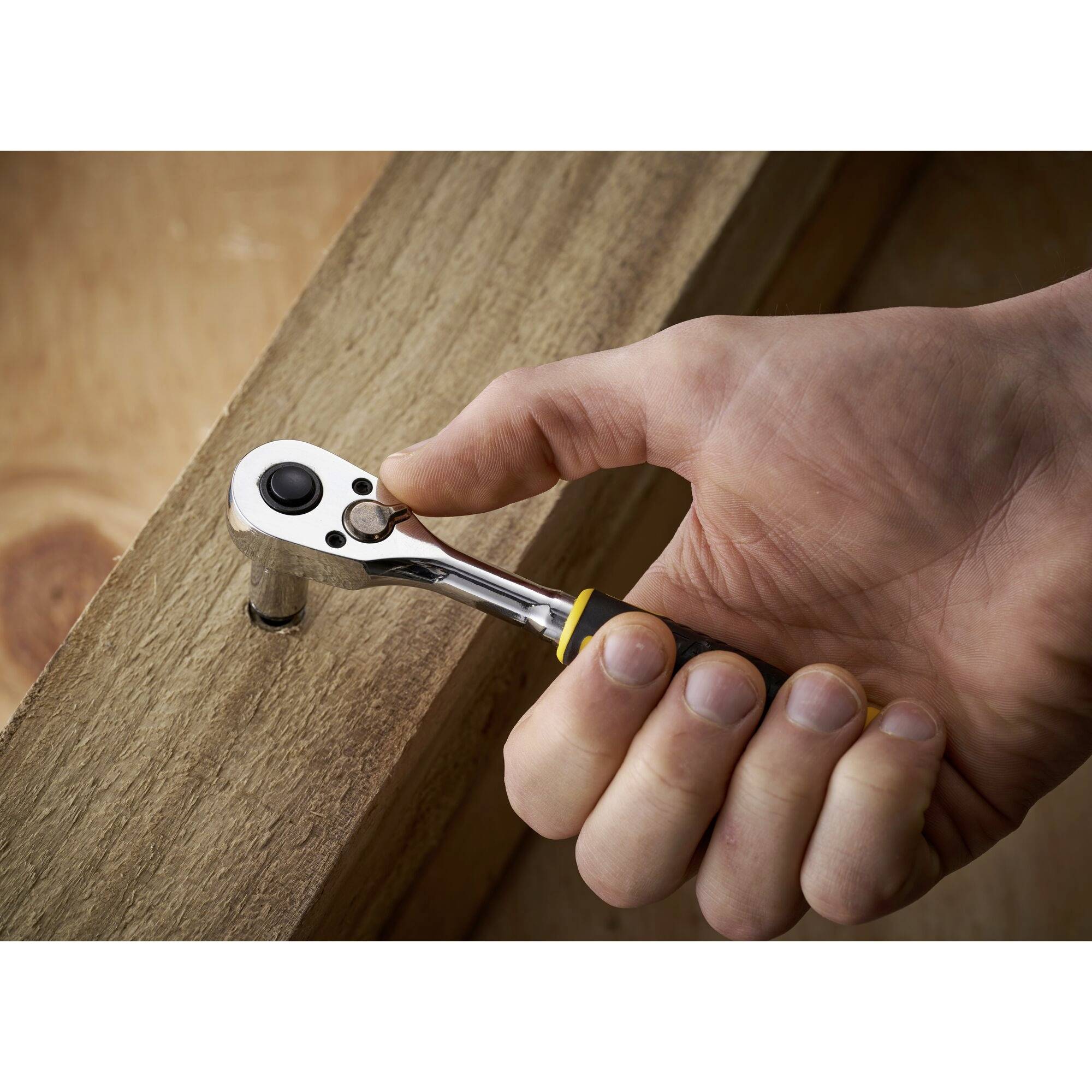 Een hand draait met een ratelsteeksleutel een schroef stevig in een houten plank.