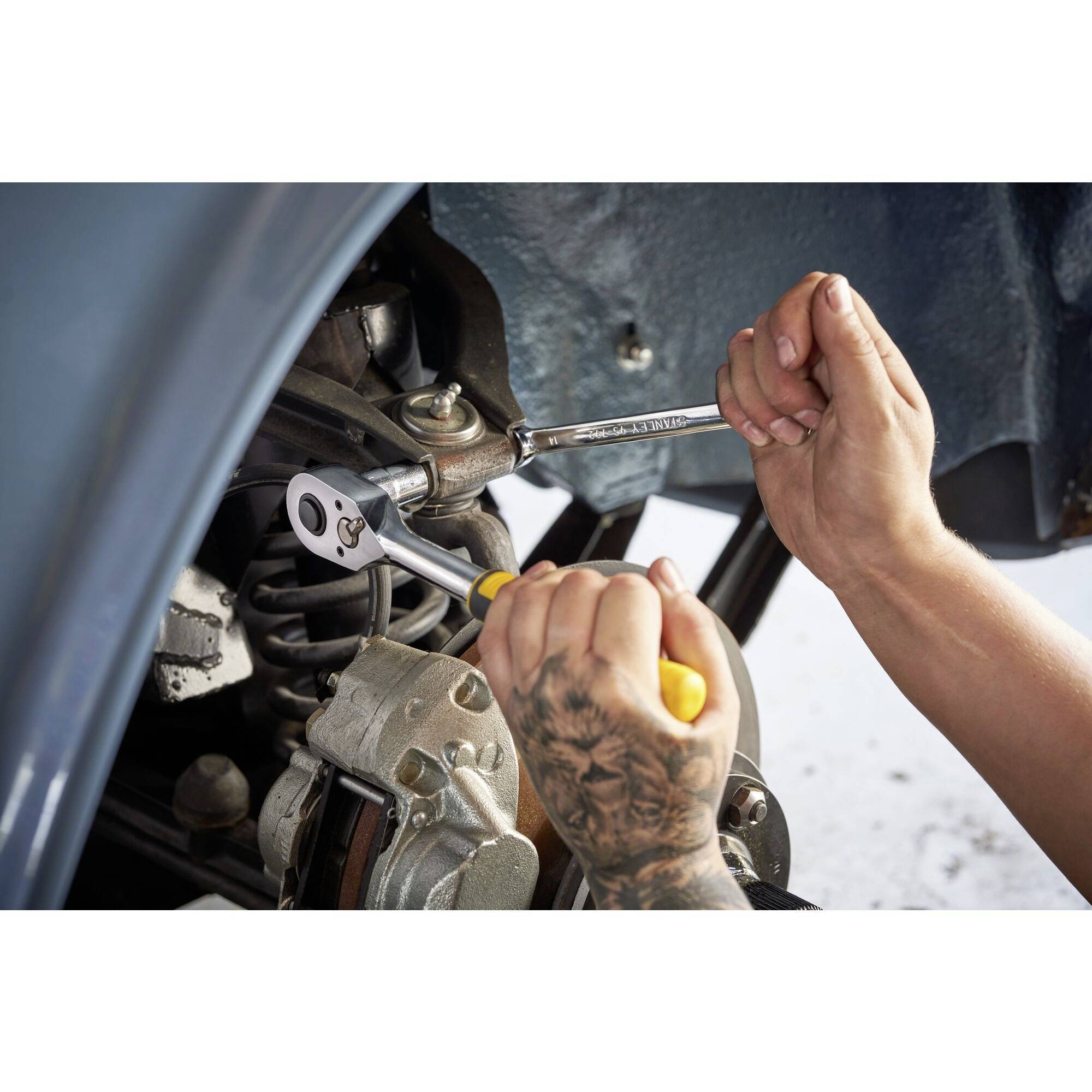 Een persoon repareert een auto, gebruikt een ratelsleutel bij het wielgedeelte. Handen met gele handschoenen tonen mechanisch werk.