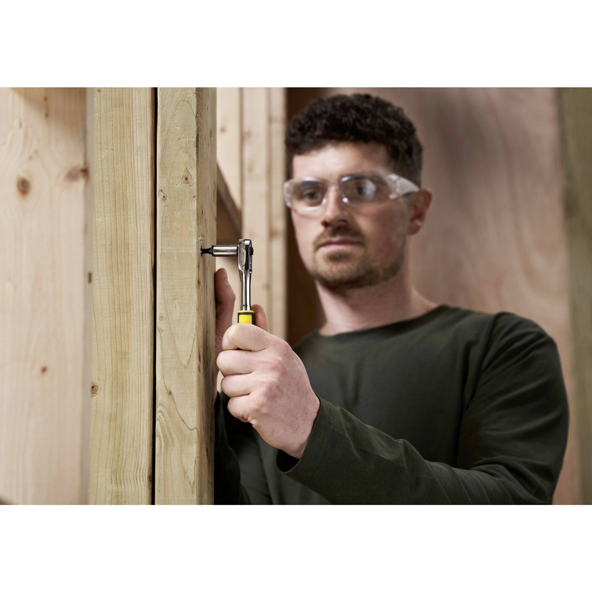 Een man met veiligheidsbril bevestigt een schroef in een houten paal met een moersleutel. Houten achtergrond.