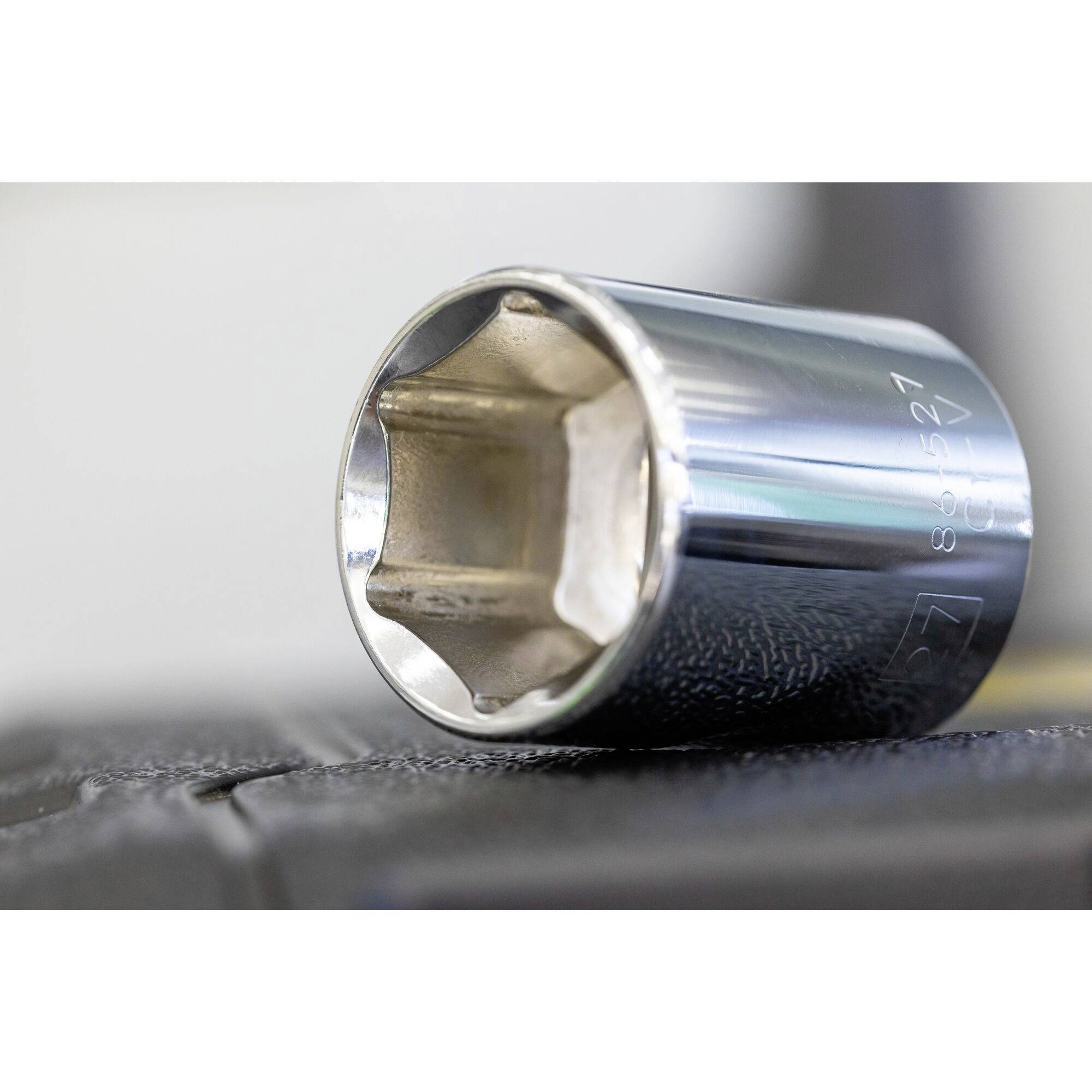 Een verchroomde dopsleutelopzetstuk ligt schuin op een donker oppervlak en toont zijn zeshoekige vorm.