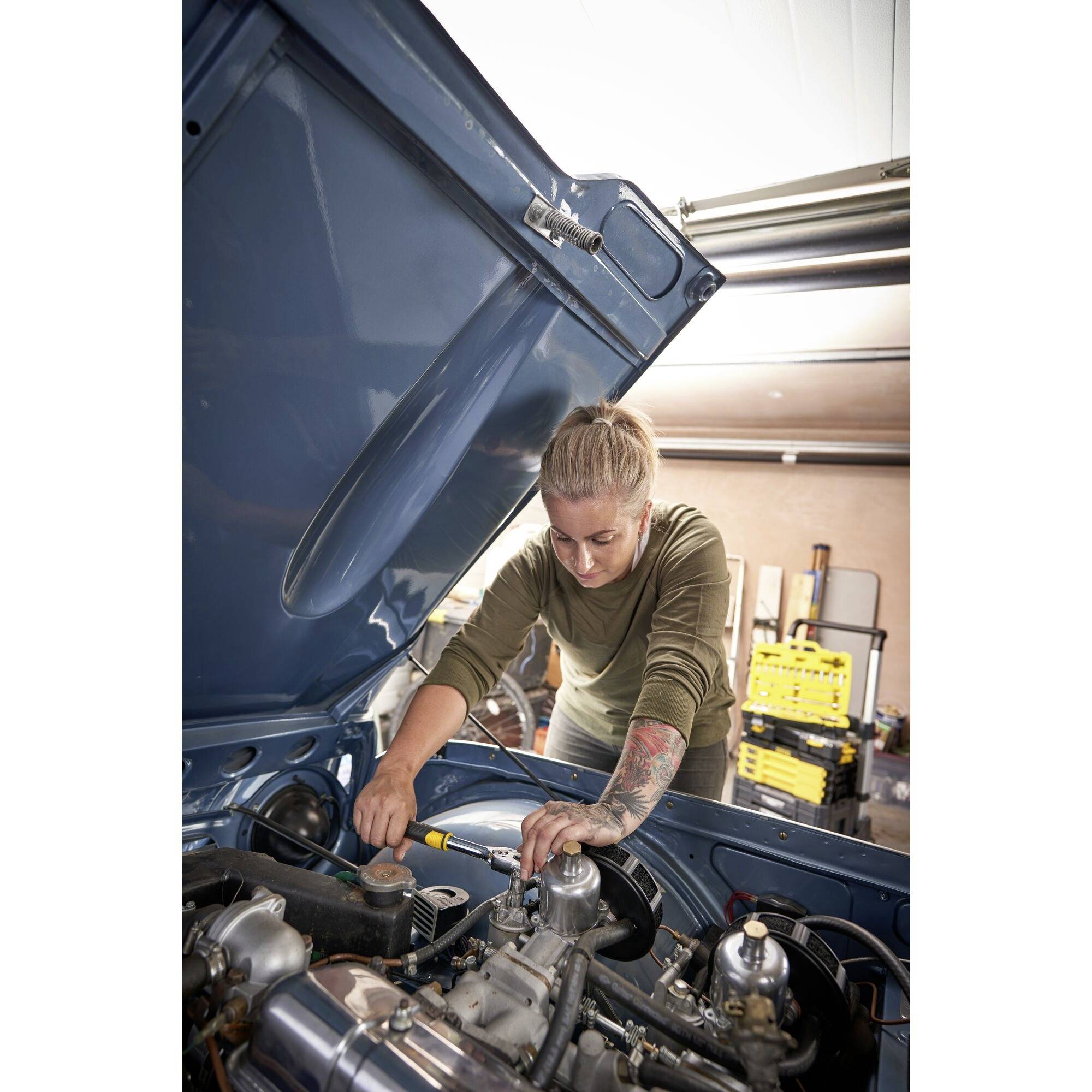 Een persoon werkt geconcentreerd aan de motor van een auto in een garage, terwijl hij met gereedschappen sleutelt en de motor controleert.