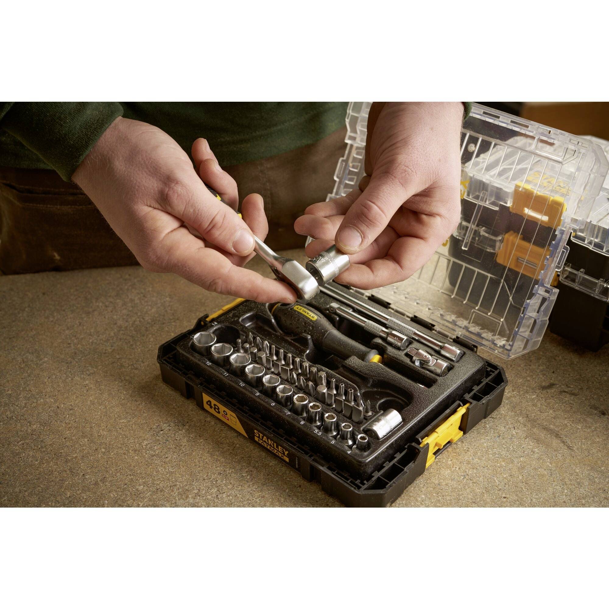 Een persoon houdt een moersleutel boven een open gereedschapskist met verschillende opzetstukken en gereedschappen.