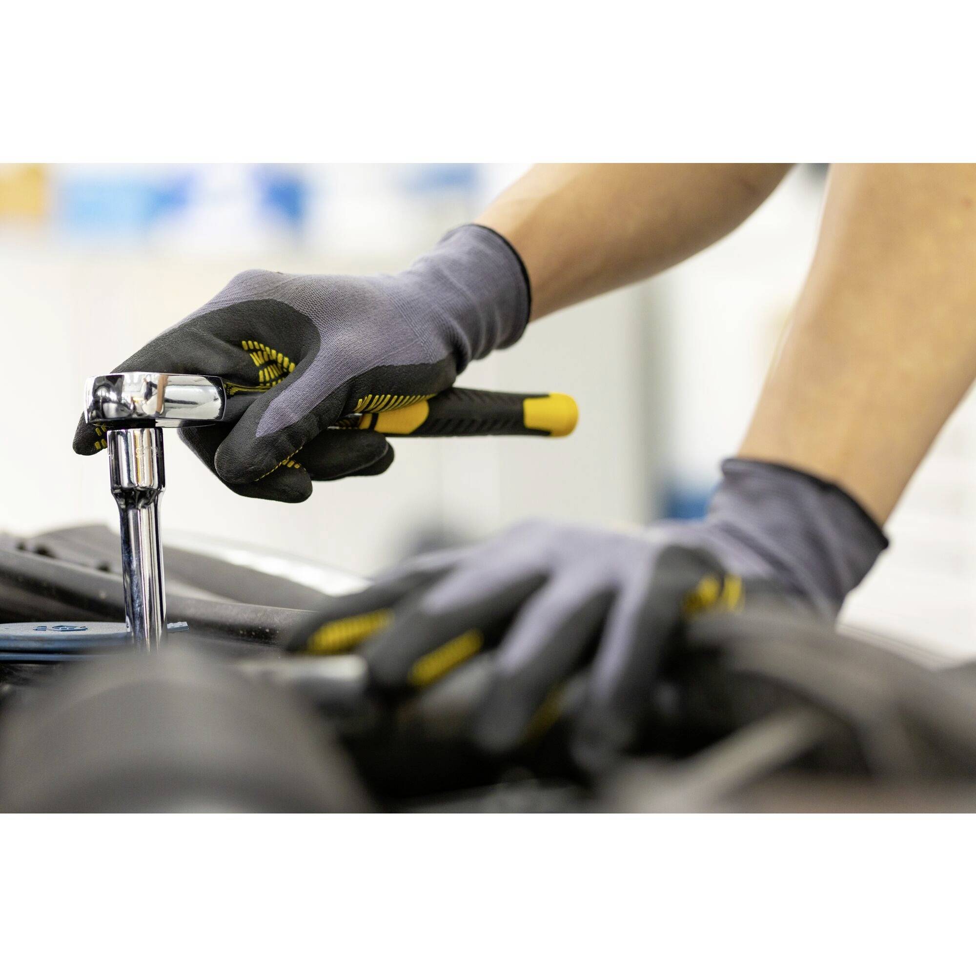 Een persoon met grijze handschoenen draait een schroef aan met een ratelsleutel aan een voertuig in een werkplaats.