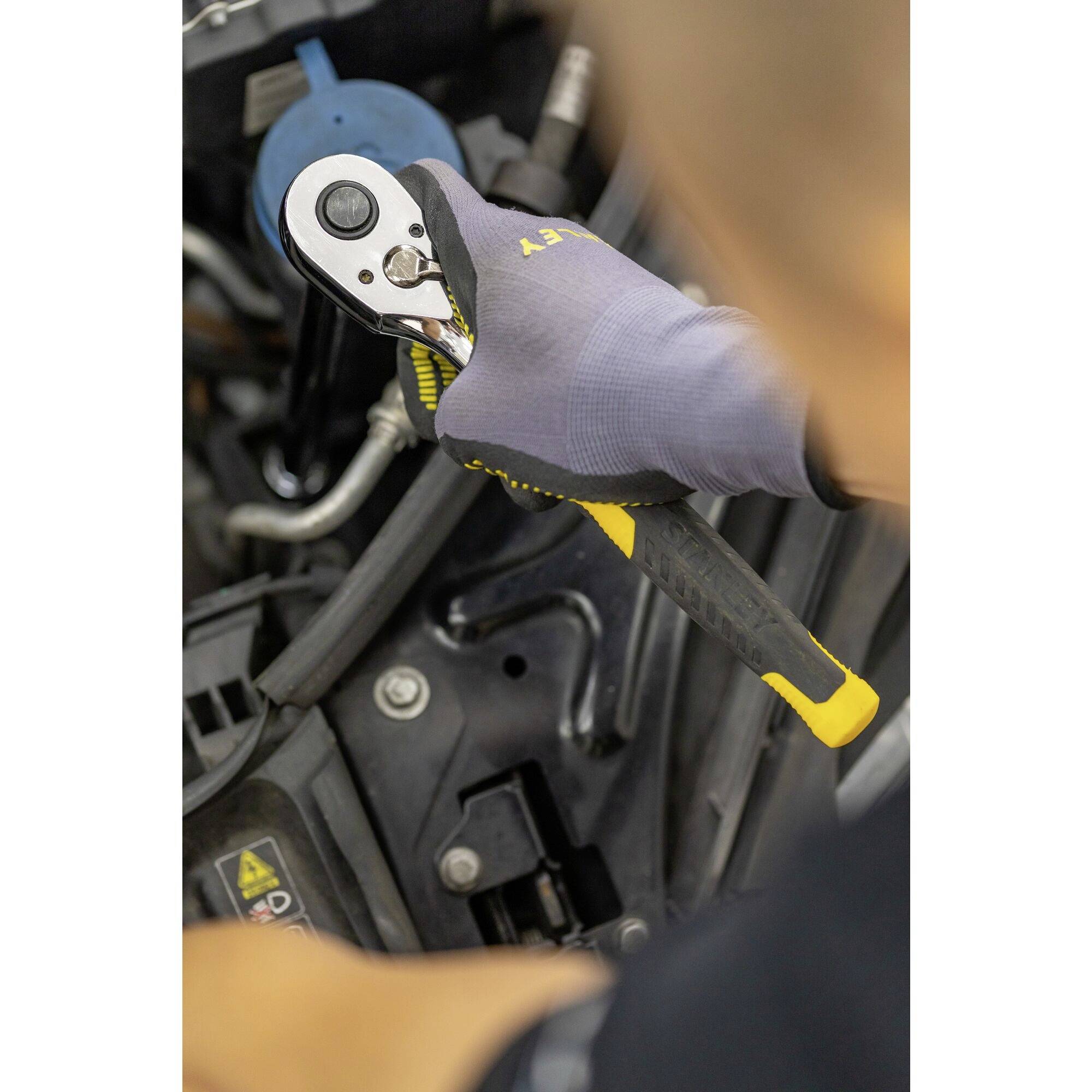 Een persoon repareert een motor, draagt handschoenen en gebruikt een ratel om een schroef vast te draaien. De focus ligt op de hand.