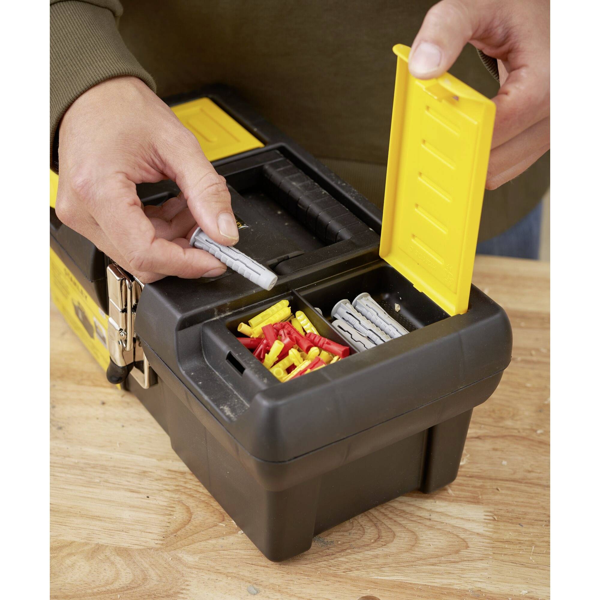 Een persoon sorteert pluggen in een zwarte gereedschapskist met een gele deksel. De pluggen zijn grijs en rood.