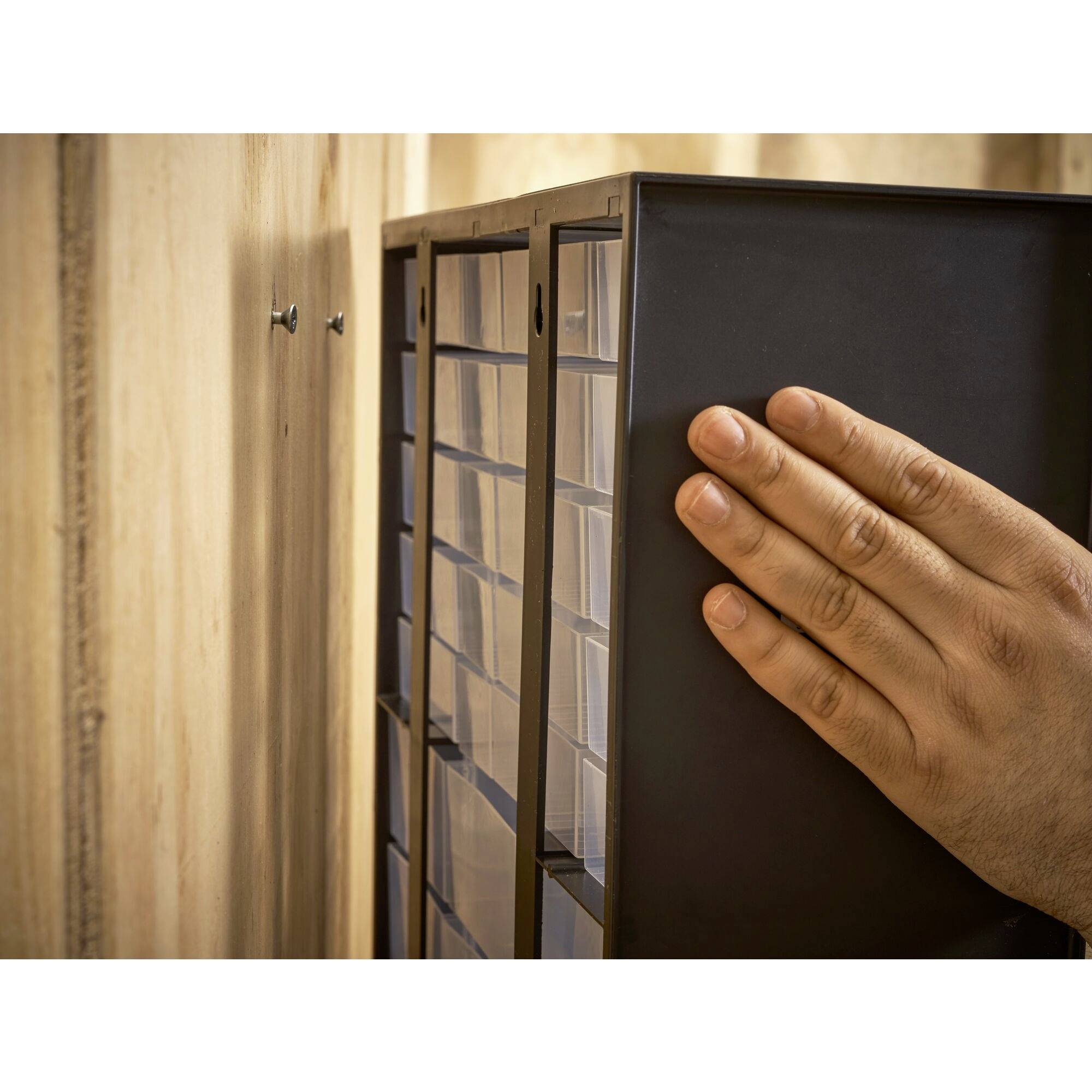 Met de hand gemonteerde zwarte metalen kooi aan een houten muur met schroeven, toont stap in het bevestigingsproces van een rek.