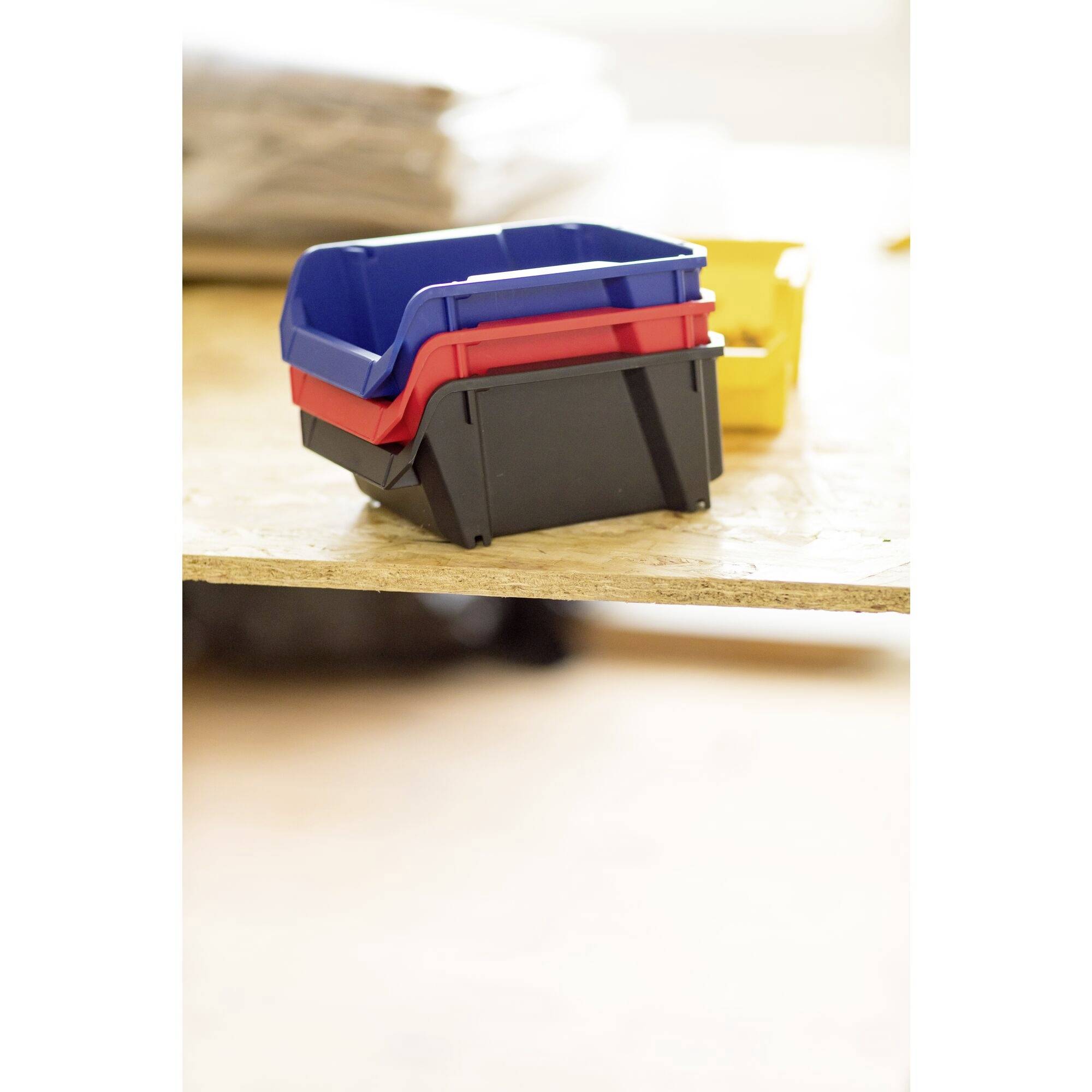 'Drie gestapelde kunststof containers in blauw, rood en zwart op een tafel, achtergrond wazig.'