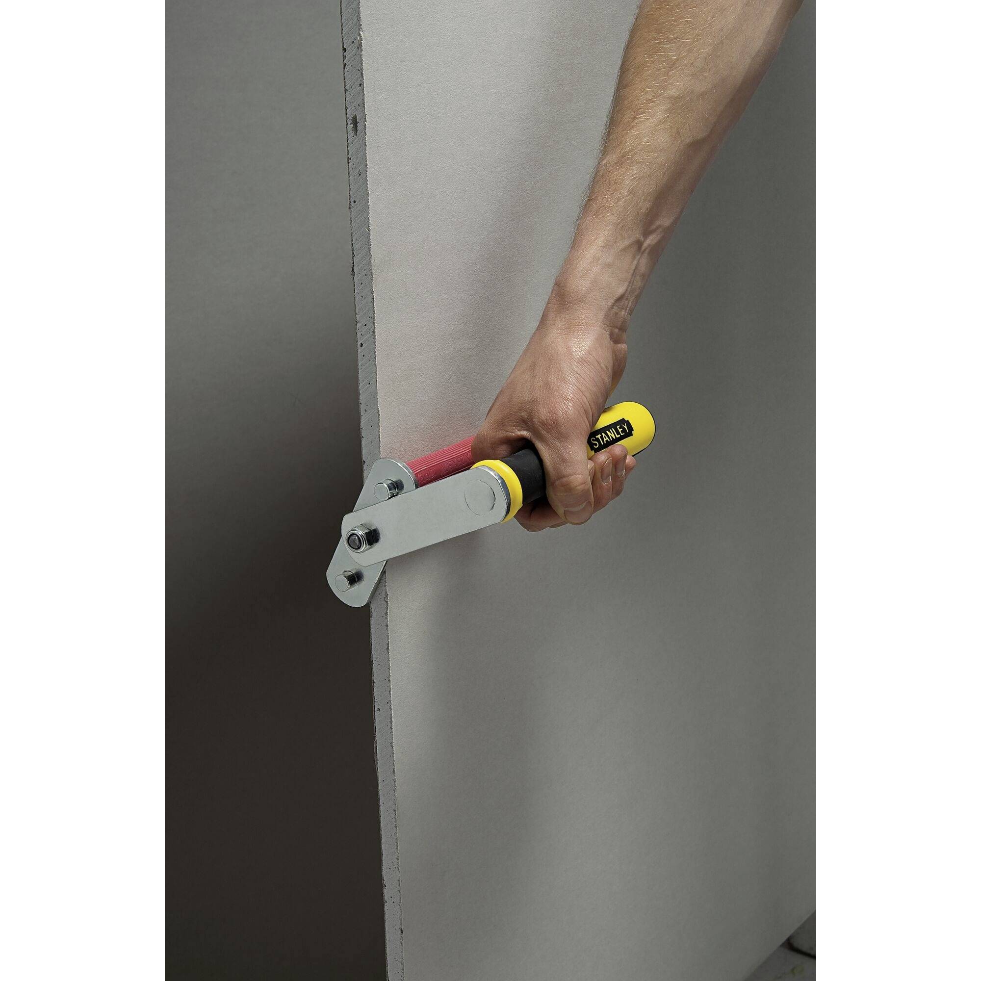 Een arm houdt een gereedschap vast dat wordt gebruikt langs de rand van een grijze plaat. Het lijkt een randbewerkingereedschap te zijn.