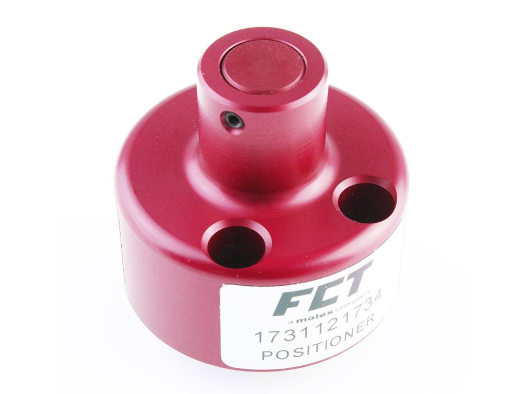Rood cilindrisch metalen apparaat met het opschrift 'FCT', serienummer 173112734. Twee langwerpige gaten op het oppervlak.