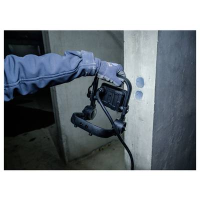Handschoenen dragende werkman die een handheld boor- of inspectiewerktuig op een betonnen muur gebruikt naast twee ronde gaten.