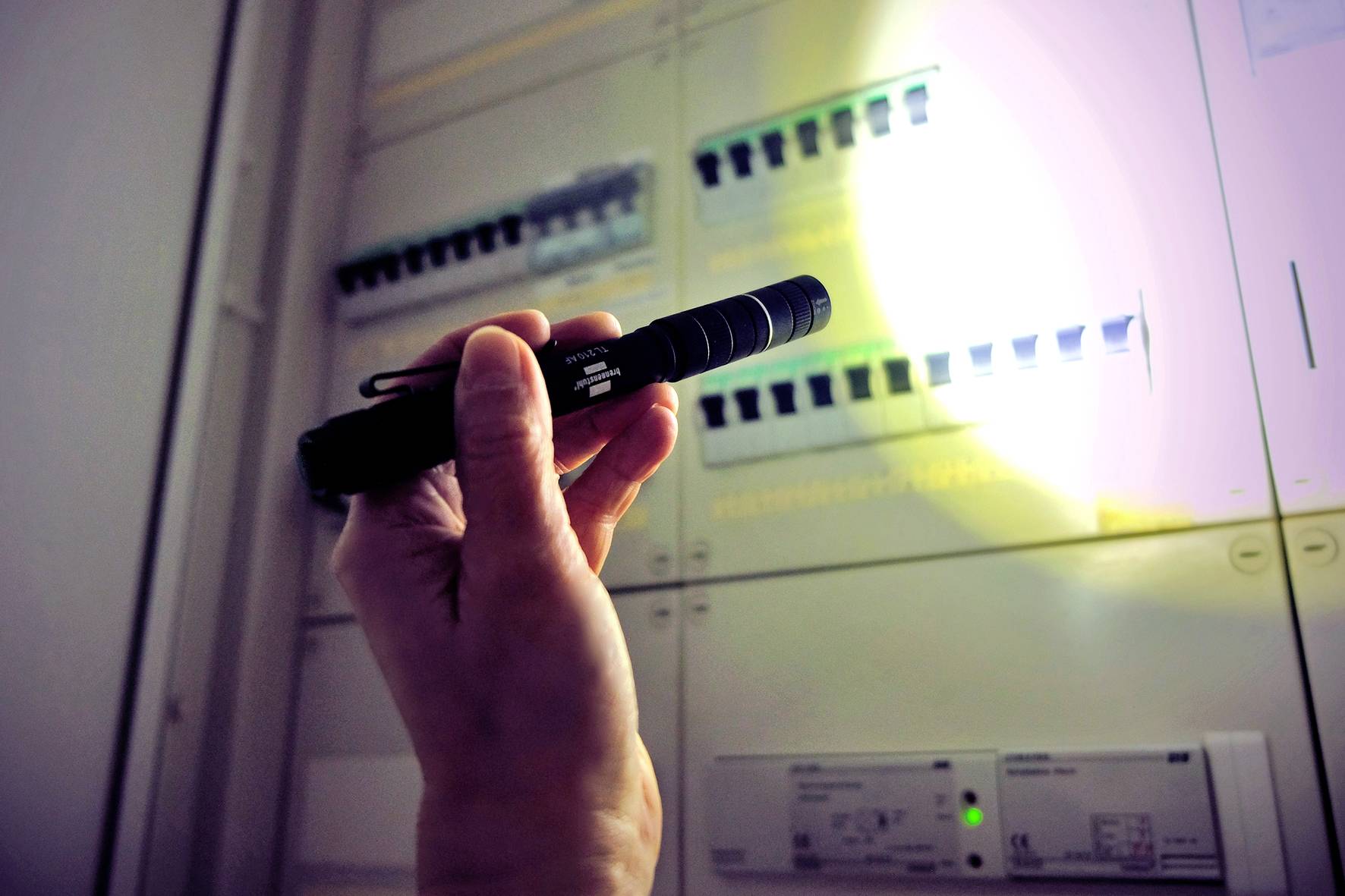 Een hand houdt een zaklamp vast en schijnt op een zekeringenkast. De focus ligt op de zekeringen om details waar te nemen.