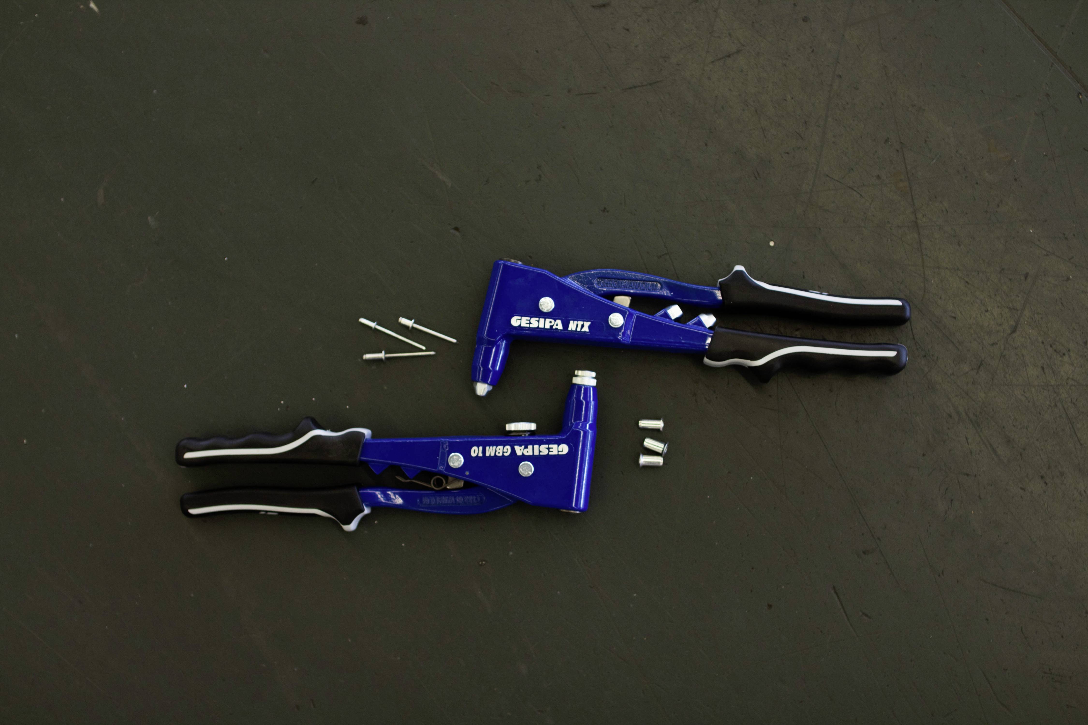 Twee blauwe nijptangen, één met drie klinknagels en de andere met twee bekken, liggen op een donkere achtergrond.