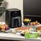 Een zwarte airfryer op een tafel naast verschillende gerechten. Een badge toont '70% minder energieverbruik'.