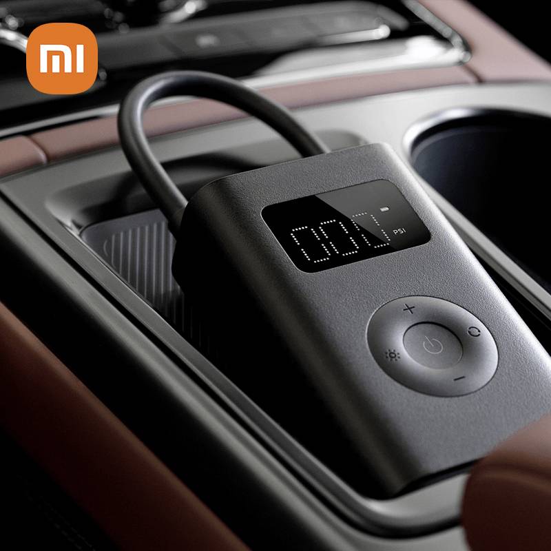 Een draagbare luchtcompressor van Xiaomi ligt op een dashboardvak van een auto, met digitale weergave en bedieningsknoppen zichtbaar.