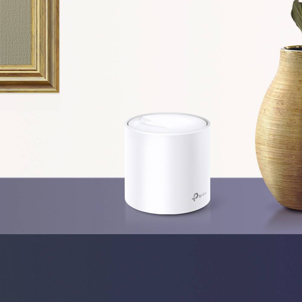 Een witte, cilindrische luidspreker op een tafel naast een bruine vaas en een ingelijste afbeelding aan de muur.