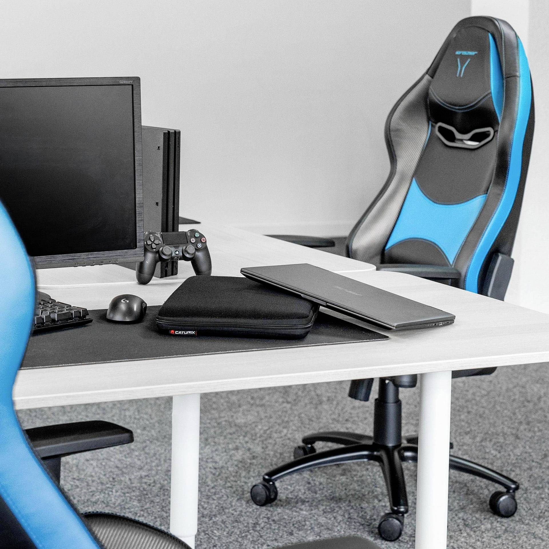 Een moderne werkplek met twee gaming-stoelen, een computerscherm, een toetsenbord, een muis en een controller op een bureau.