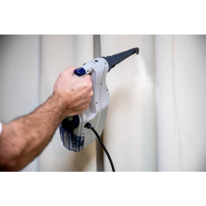 Een persoon reinigt een gordijn met een stoomreiniger. De hand houdt het apparaat vast dat stoom op de stof afgeeft.