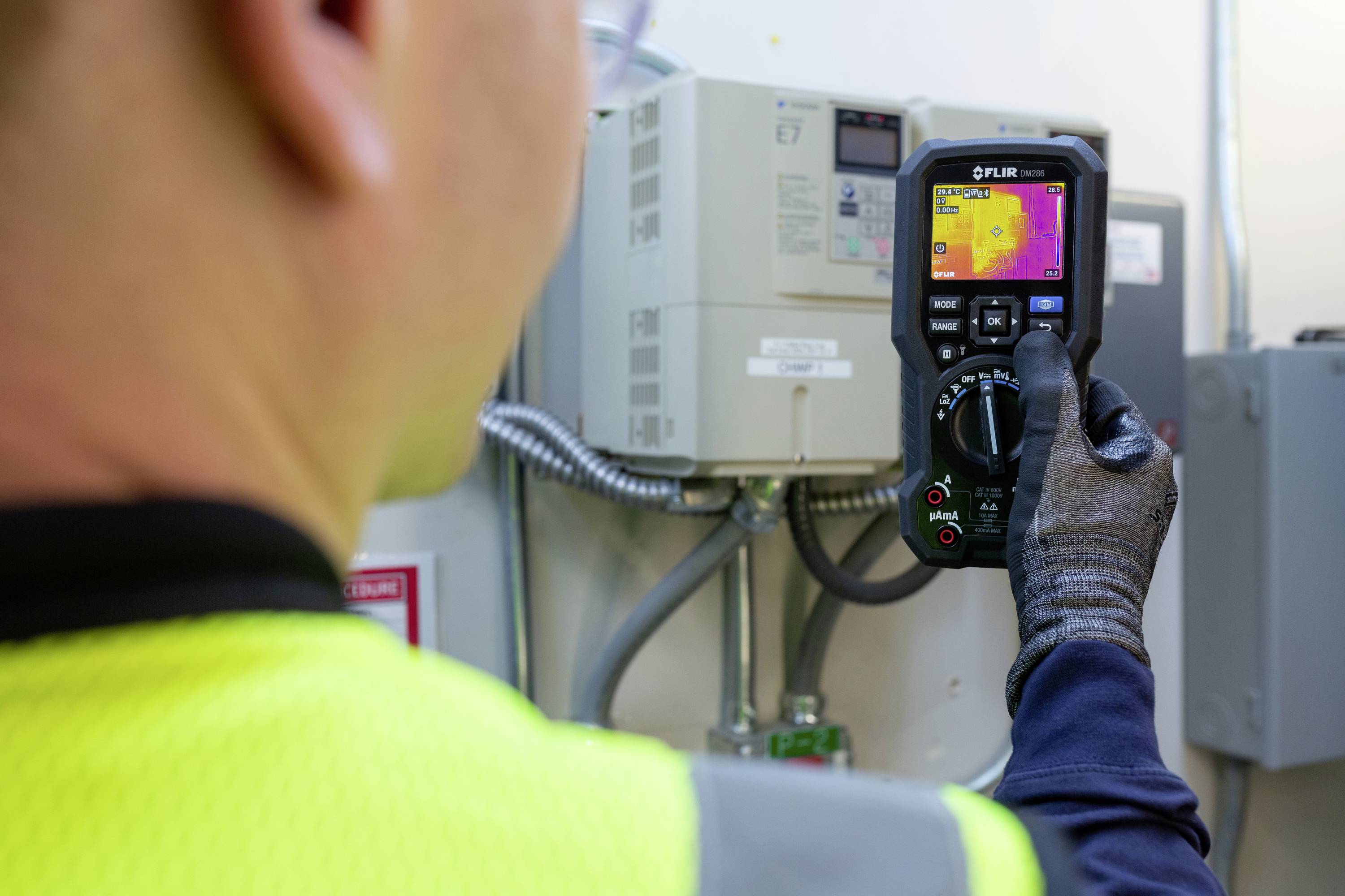 Een persoon in veiligheidskleding gebruikt een warmtebeeldcamera om de temperatuur van een elektrisch apparaat te controleren.