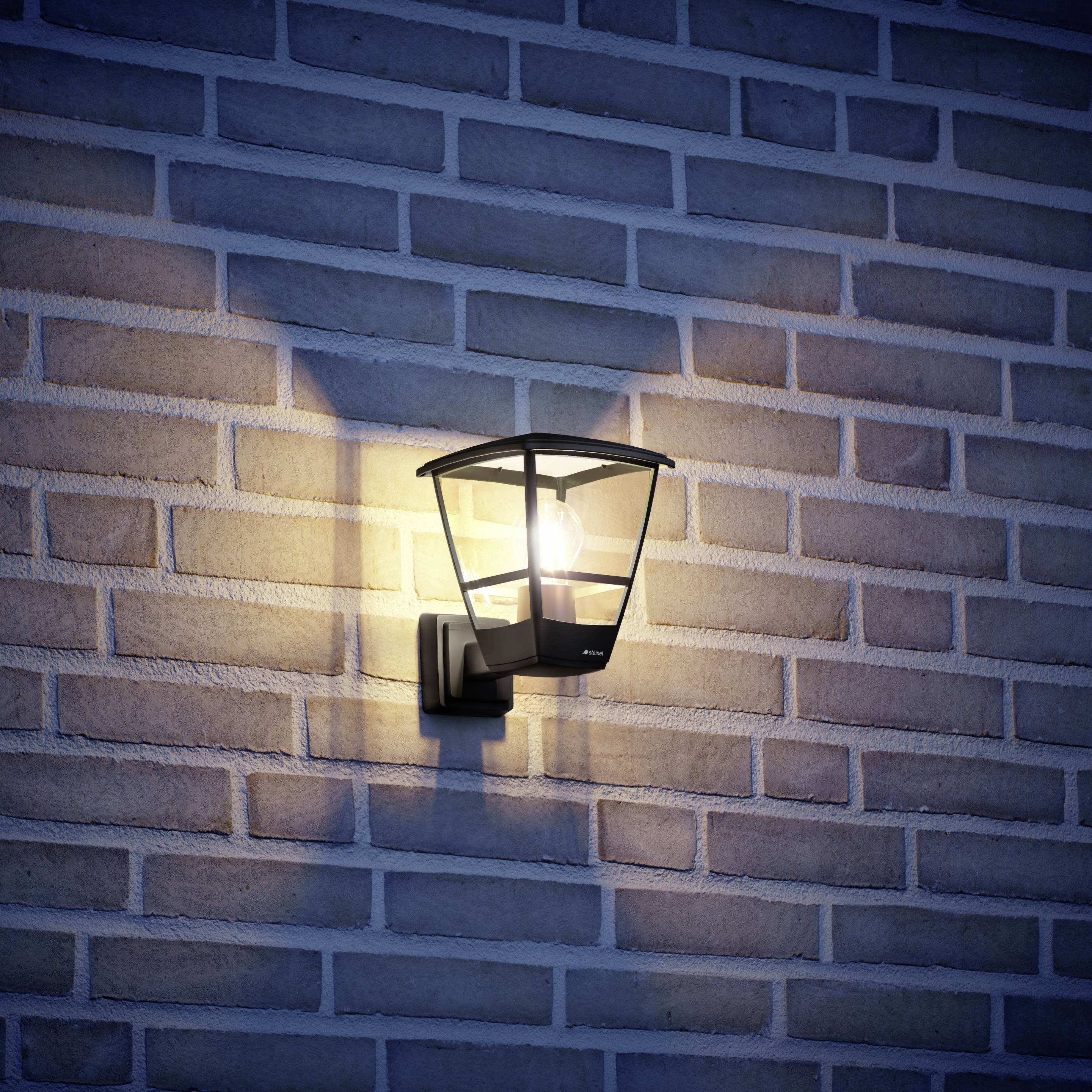 Wandlamp aan bakstenen muur, verspreidt warm licht in de schemering.