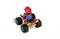 Een speelgoedfiguur in een rood kostuum en muts op een voertuig met vier wielen dat lijkt op een go-kart. De achtergrond is wit.