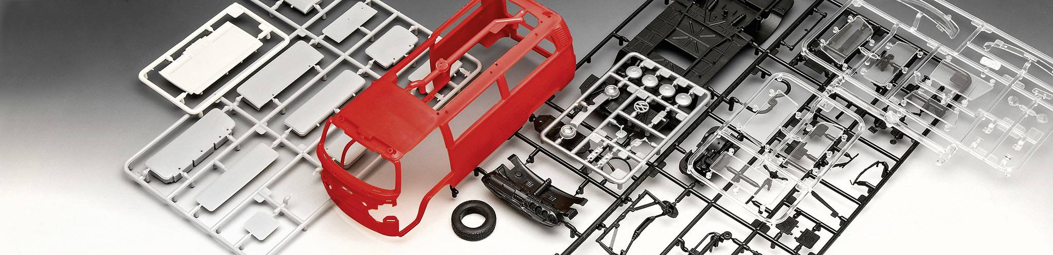 Een modelbouwset van een rode bestelwagen, met verschillende onderdelen en frame uitgespreid op een tafel.