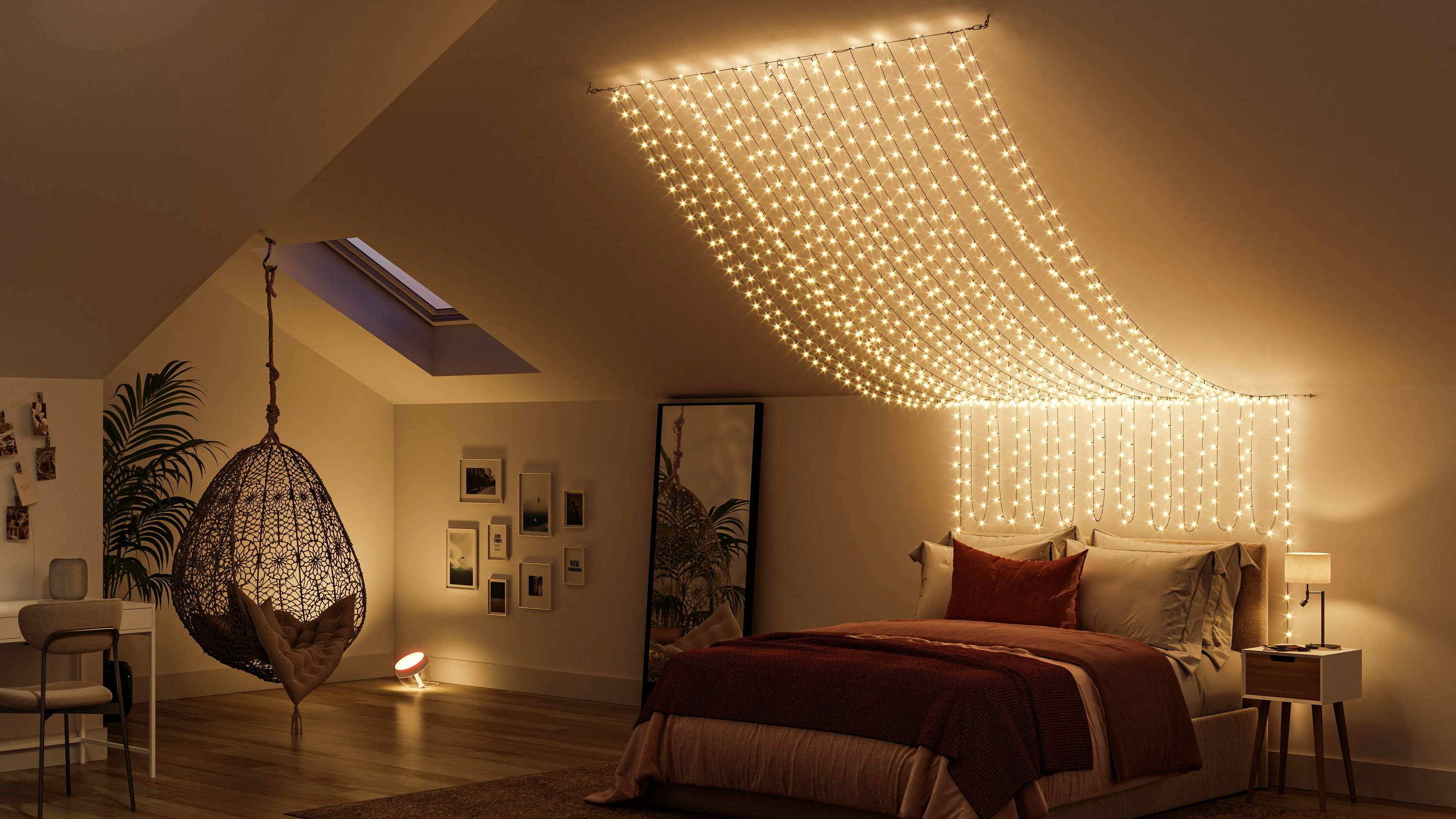 Gezellige slaapkamer met een schuin plafond, warme lichtslingers boven het bed, een hangstoel en moderne decoratie.