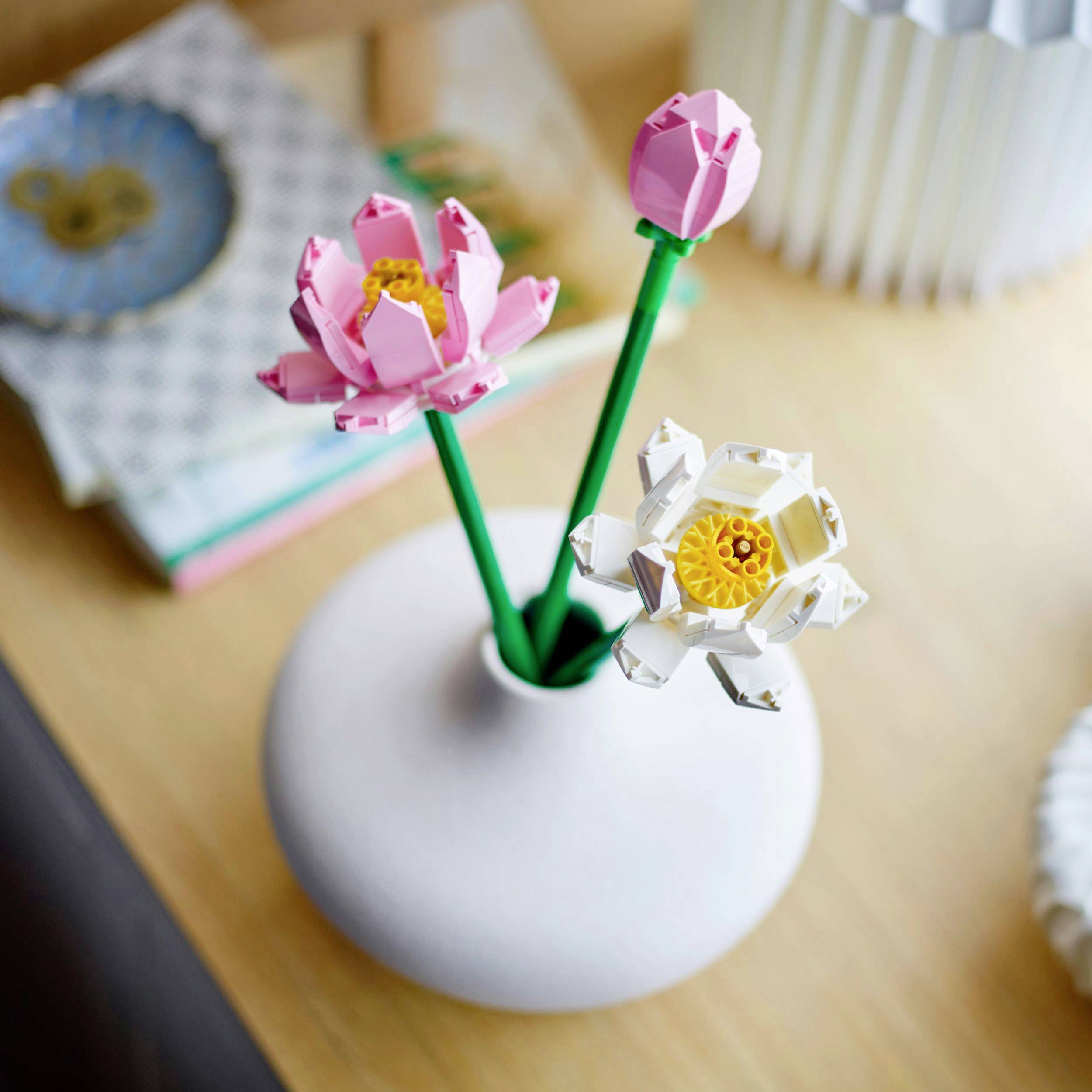 Twee kleurrijke Lego-bloemen in een witte vaas op een houten tafel, decoratief geschikt voor een onscherpe achtergrond.
