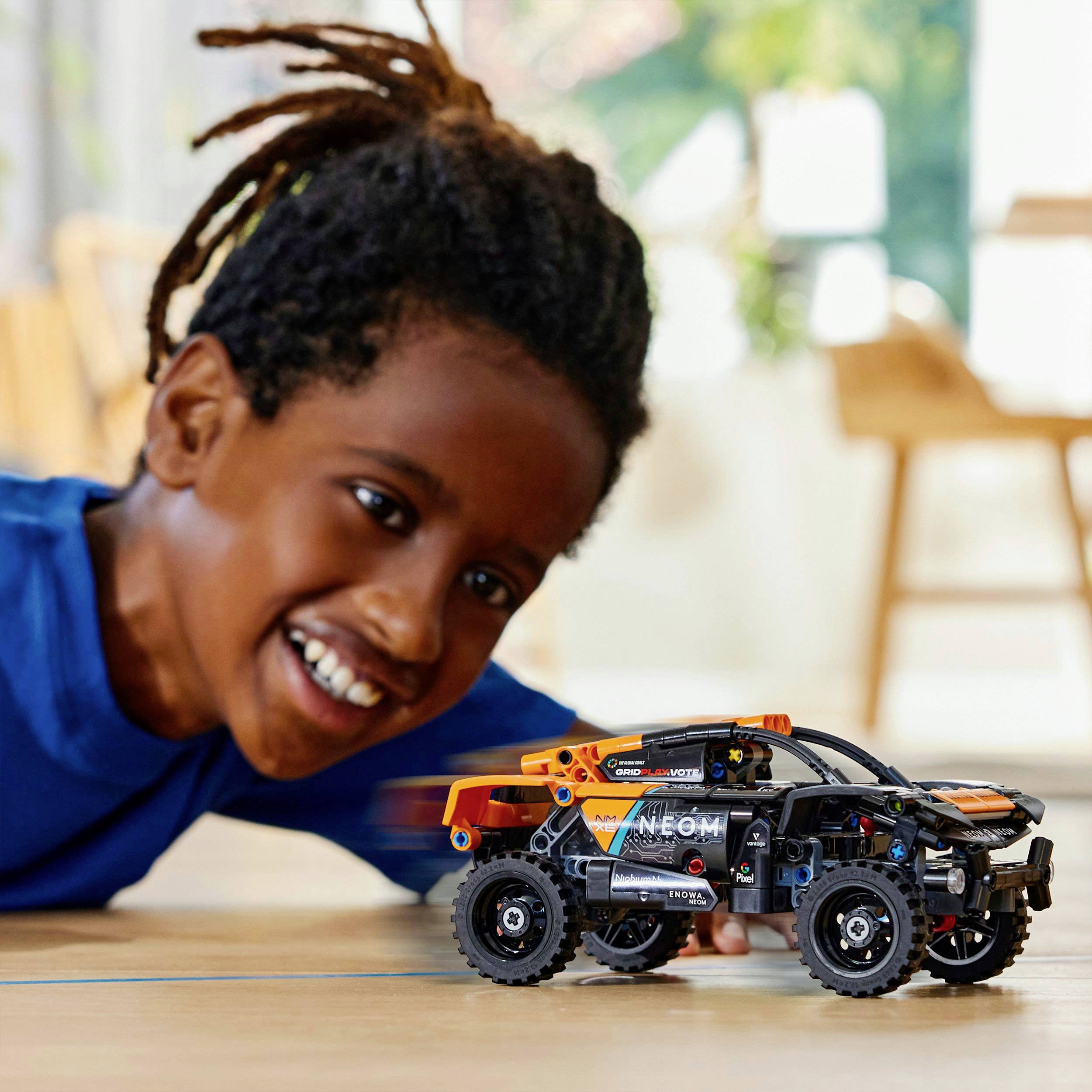 Een kind speelt gelukkig op de vloer met een kleine, moderne speelgoedauto. Op de achtergrond zijn wazig meubilair te zien.