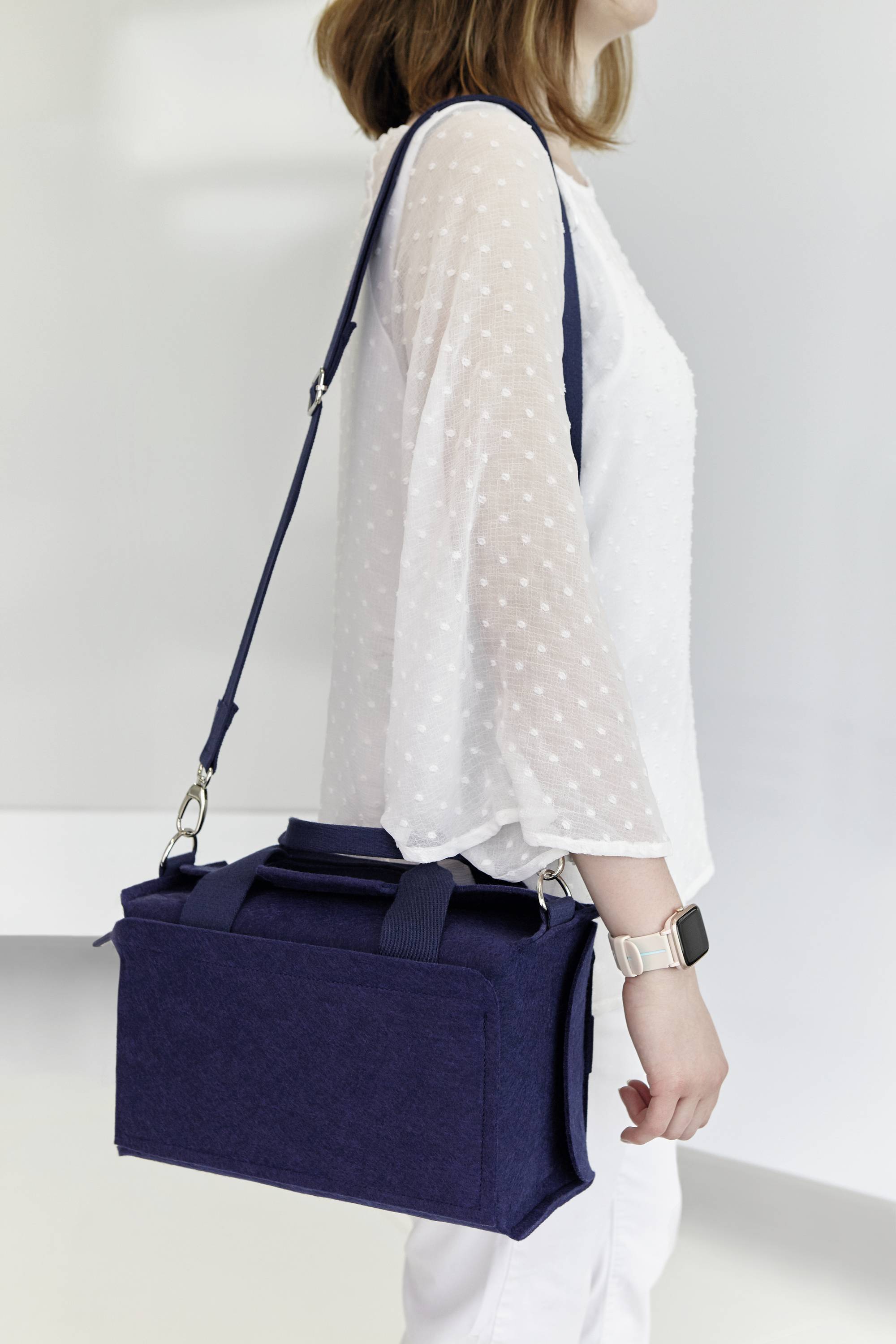 Een persoon draagt een donkerblauwe schoudertas. Ze draagt een lichte blouse met stippen en een smartwatch.
