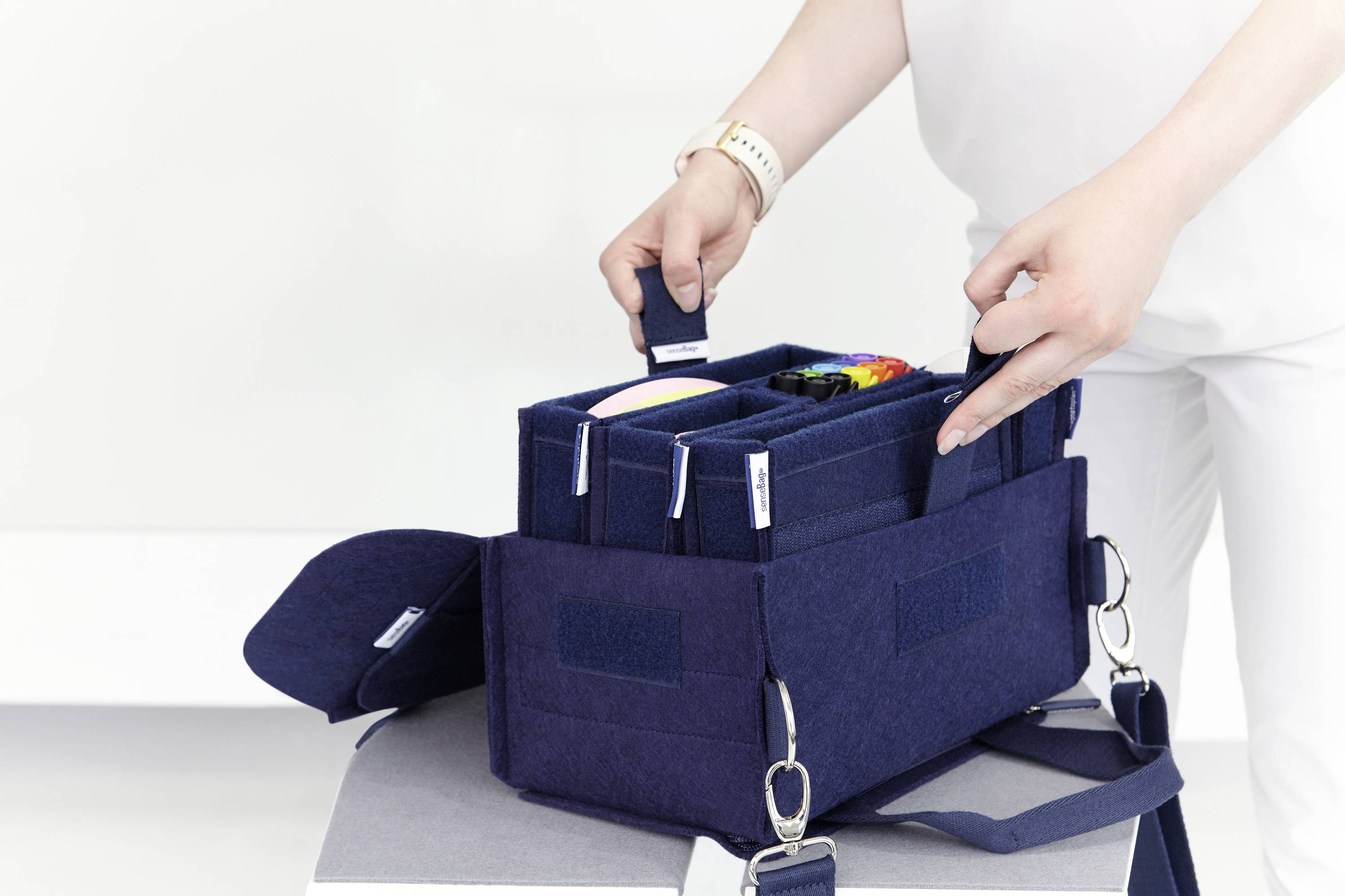 Persoon organiseert een donkerblauwe vilten tas met meerdere vakken die verschillende kleurrijke voorwerpen bevat.