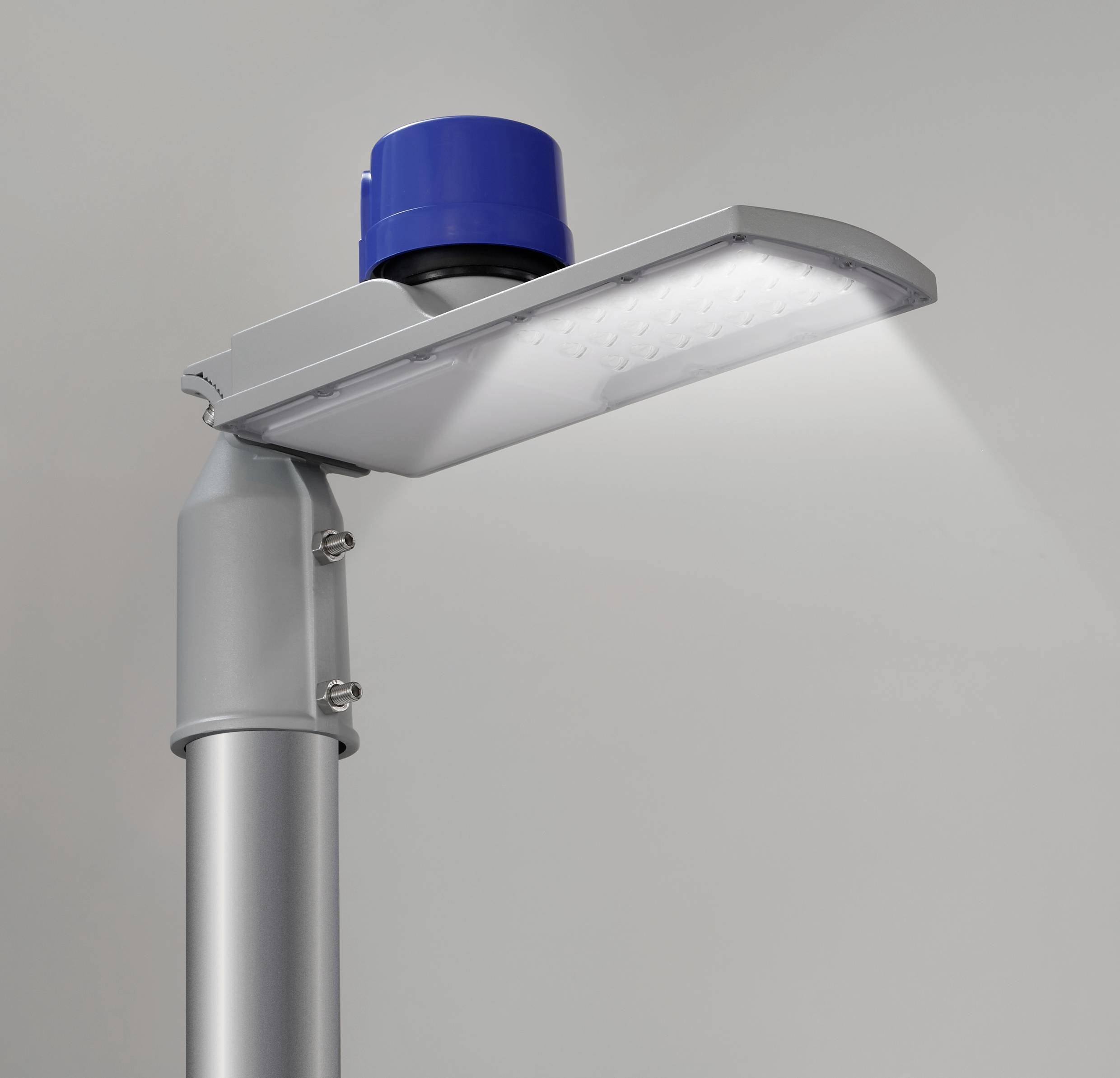 Een moderne, zilverkleurige LED-straatlantaarn met een blauwe sensor bovenaan, gemonteerd in een lichte binnenruimte en licht naar beneden schijnend.