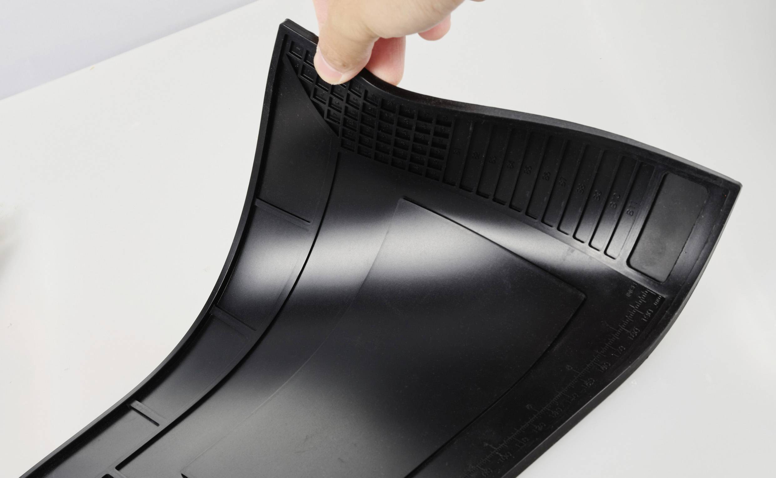 Een hand buigt een zwarte, flexibele rubbermat die op een lichte ondergrond ligt.