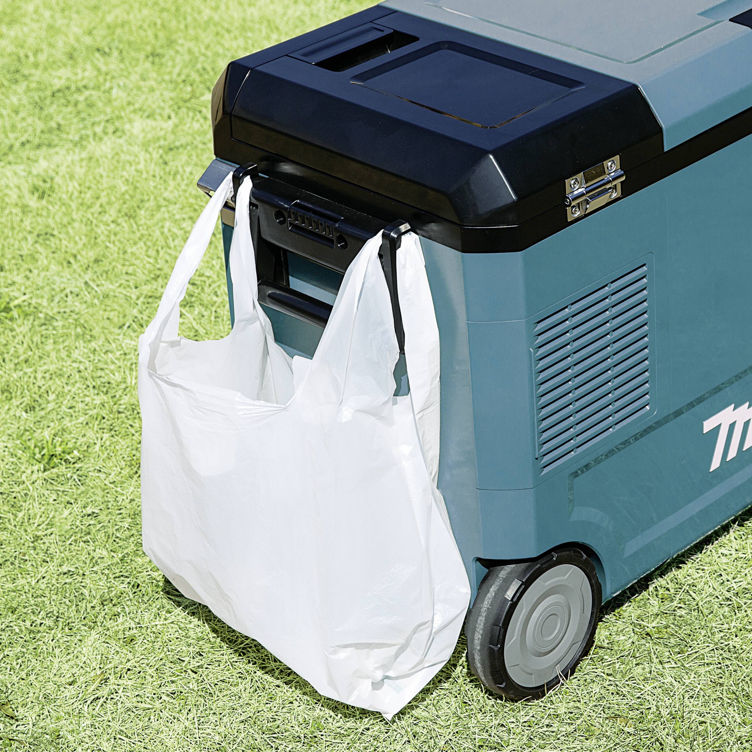 Mobiele elektrische apparaten met wielen op een grasveld, naast een opgehangen plastic tas.