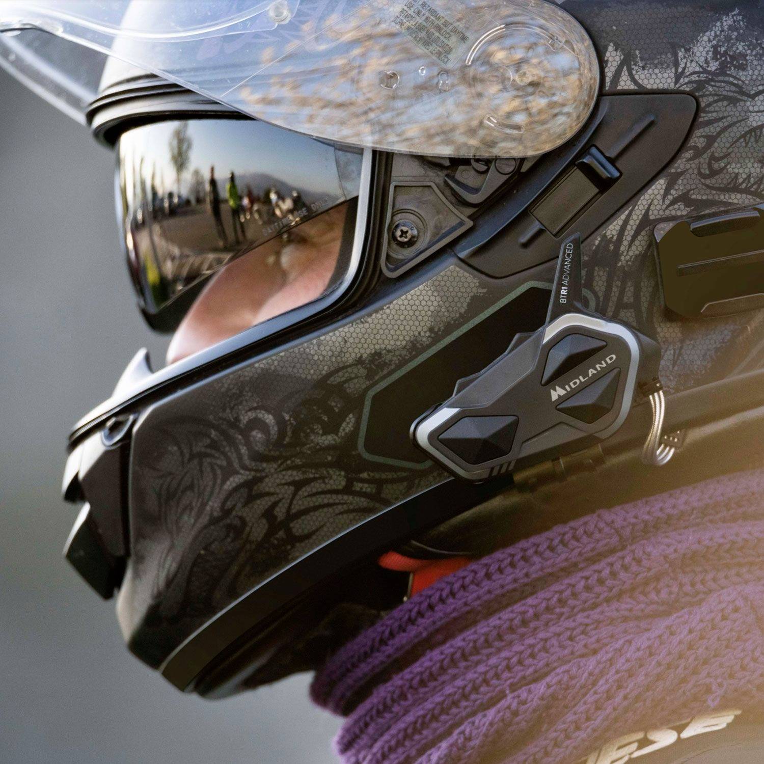 Motorhelm fotografie met open vizier, toont complexe grafische elementen en geïntegreerd communicatieapparaat aan de zijkant.