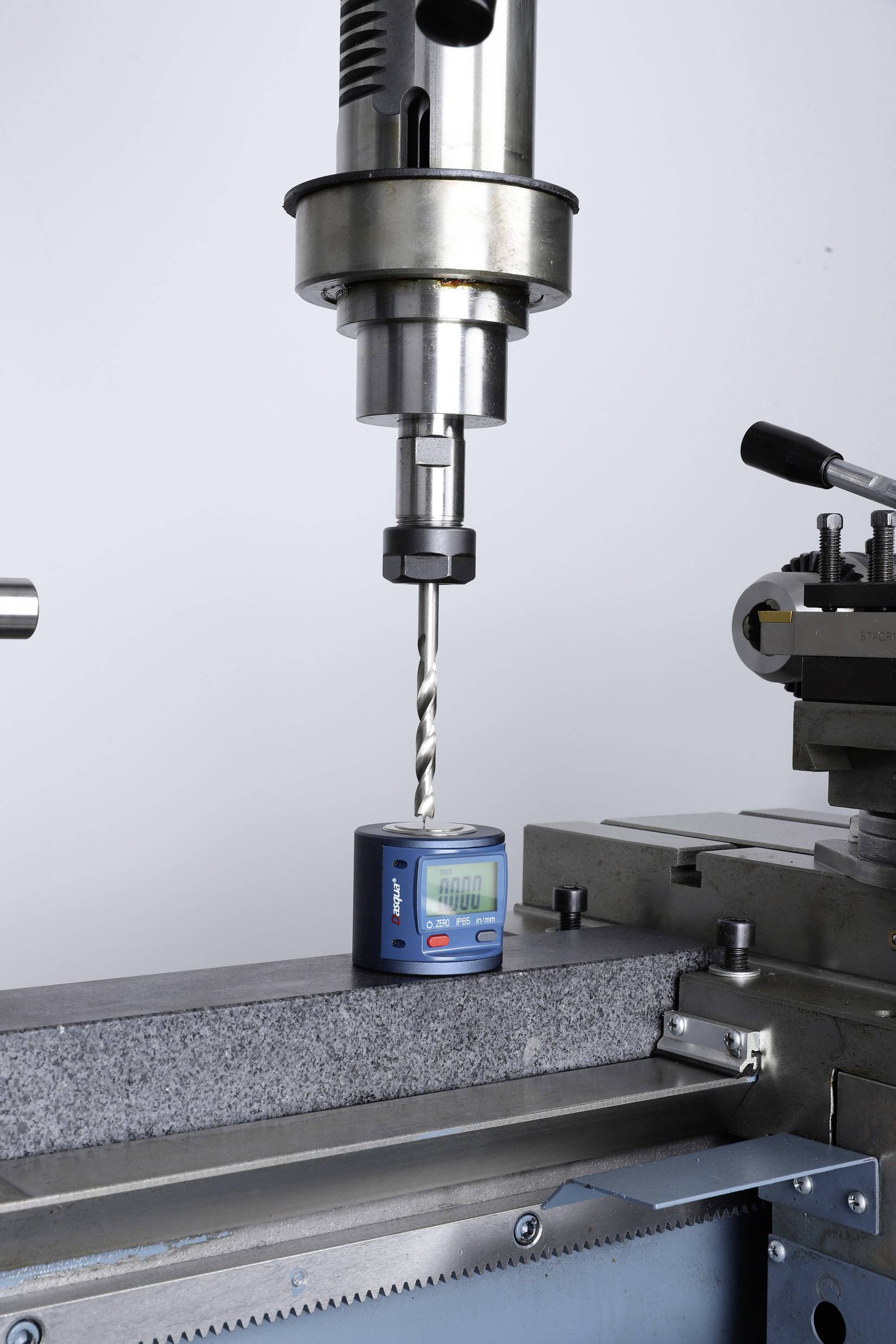 Een boor wordt gepositioneerd boven een precisie-meetinstrument dat op een metalen blok op een freesmachine ligt.