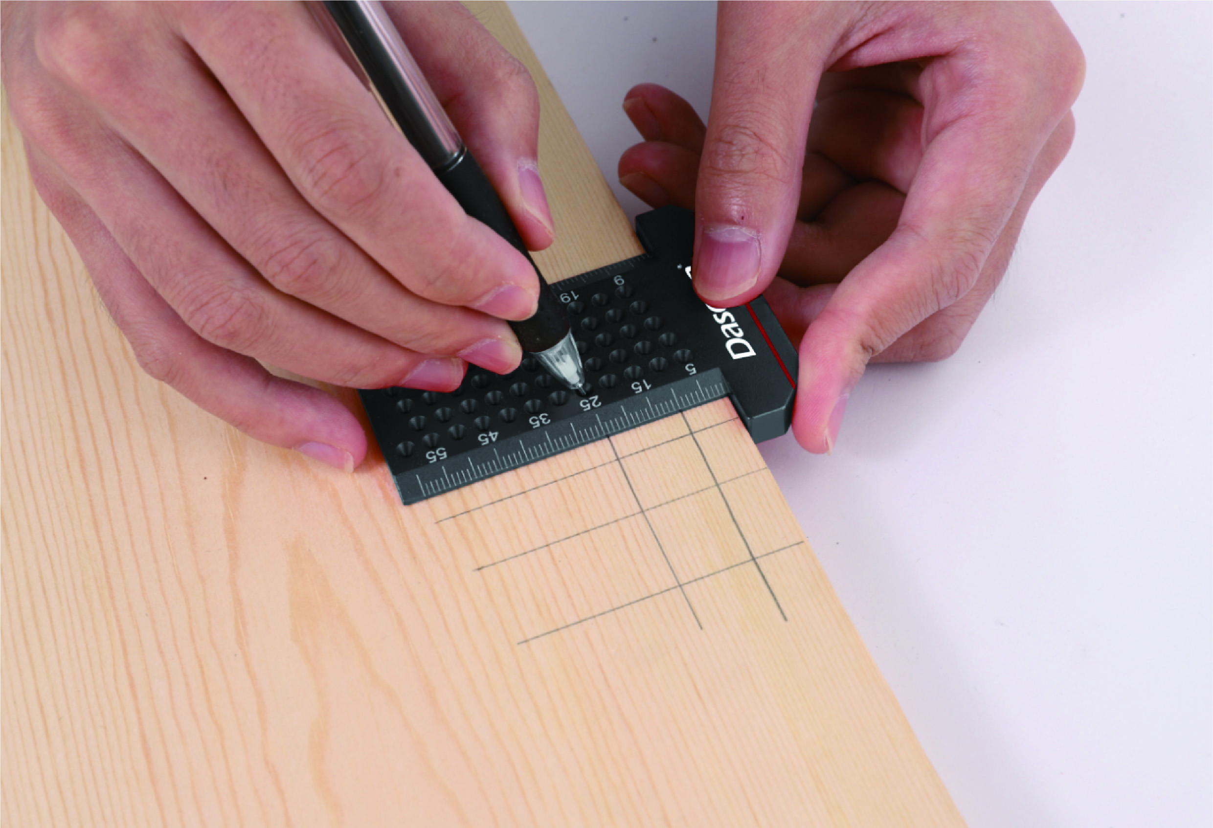 Een persoon gebruikt een liniaal en potlood om nauwkeurige lijnen op een houten plank te tekenen. Handen en gereedschappen zijn zichtbaar.