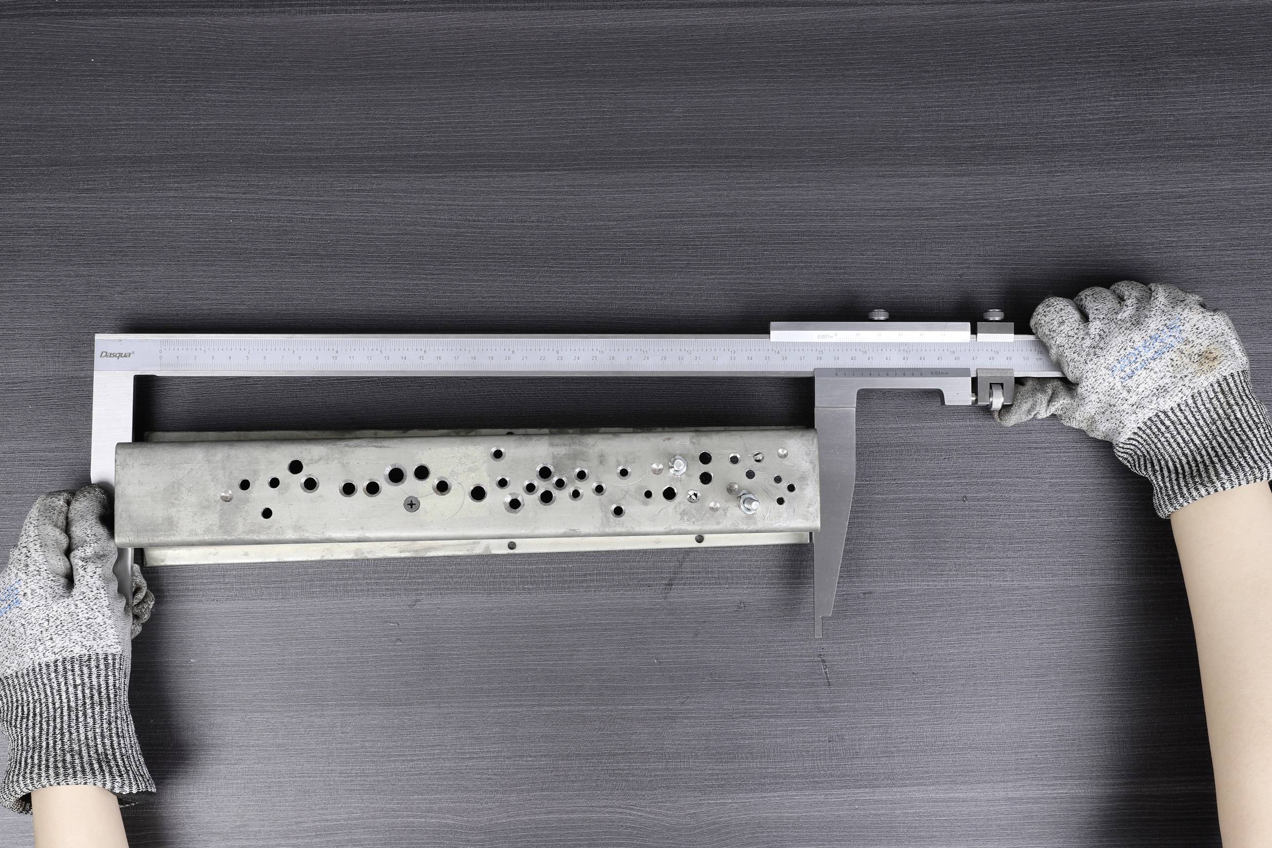 Een persoon meet een rechthoekig metalen onderdeel met een schuifmaat. Het onderdeel heeft meerdere gaten van verschillende afmetingen.